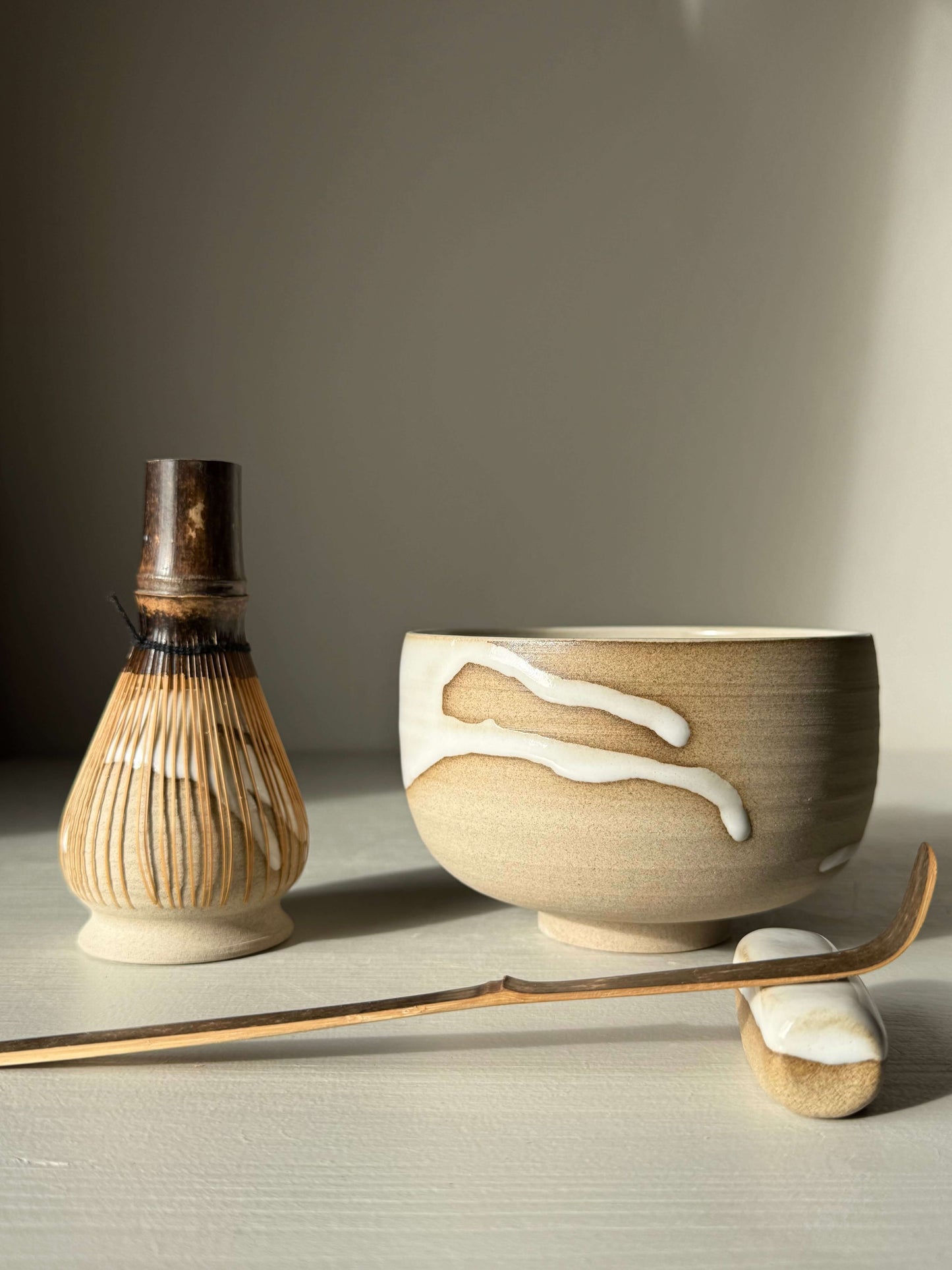 Handmade ceramic Matcha Bowl – Yuki #04 with glossy white glaze, accompanied by a bamboo whisk and scoop, part of the Yuki Series.