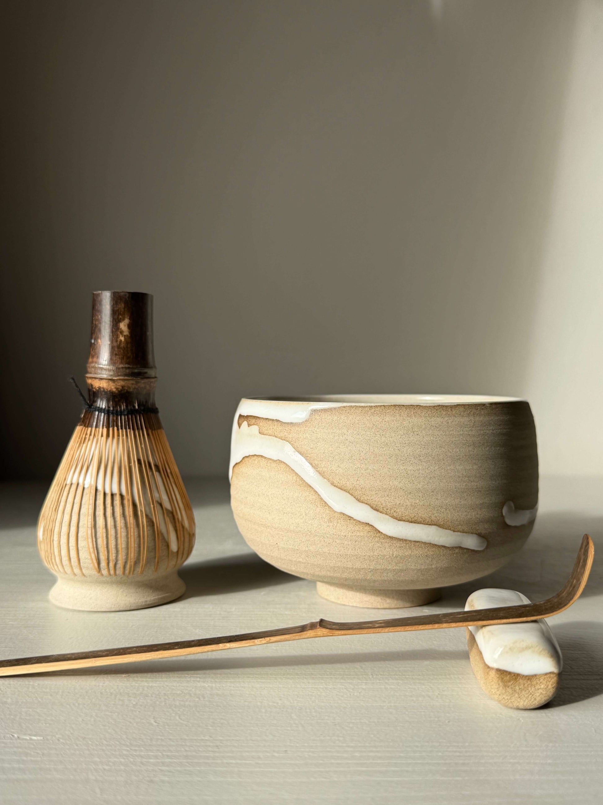 Matcha Bowl – Yuki #02, handmade ceramic with toffee clay and white glaze, next to a bamboo whisk and tea scoop, serene setting.