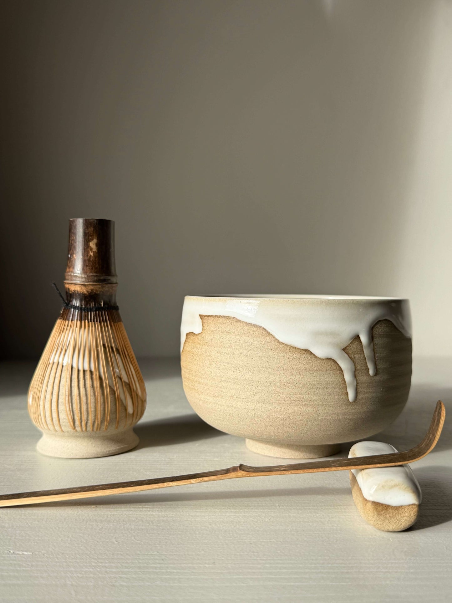 Matcha Bowl – Yuki #01, handmade ceramic bowl with glossy white glaze and toffee clay, shown with traditional matcha whisk and scoop.