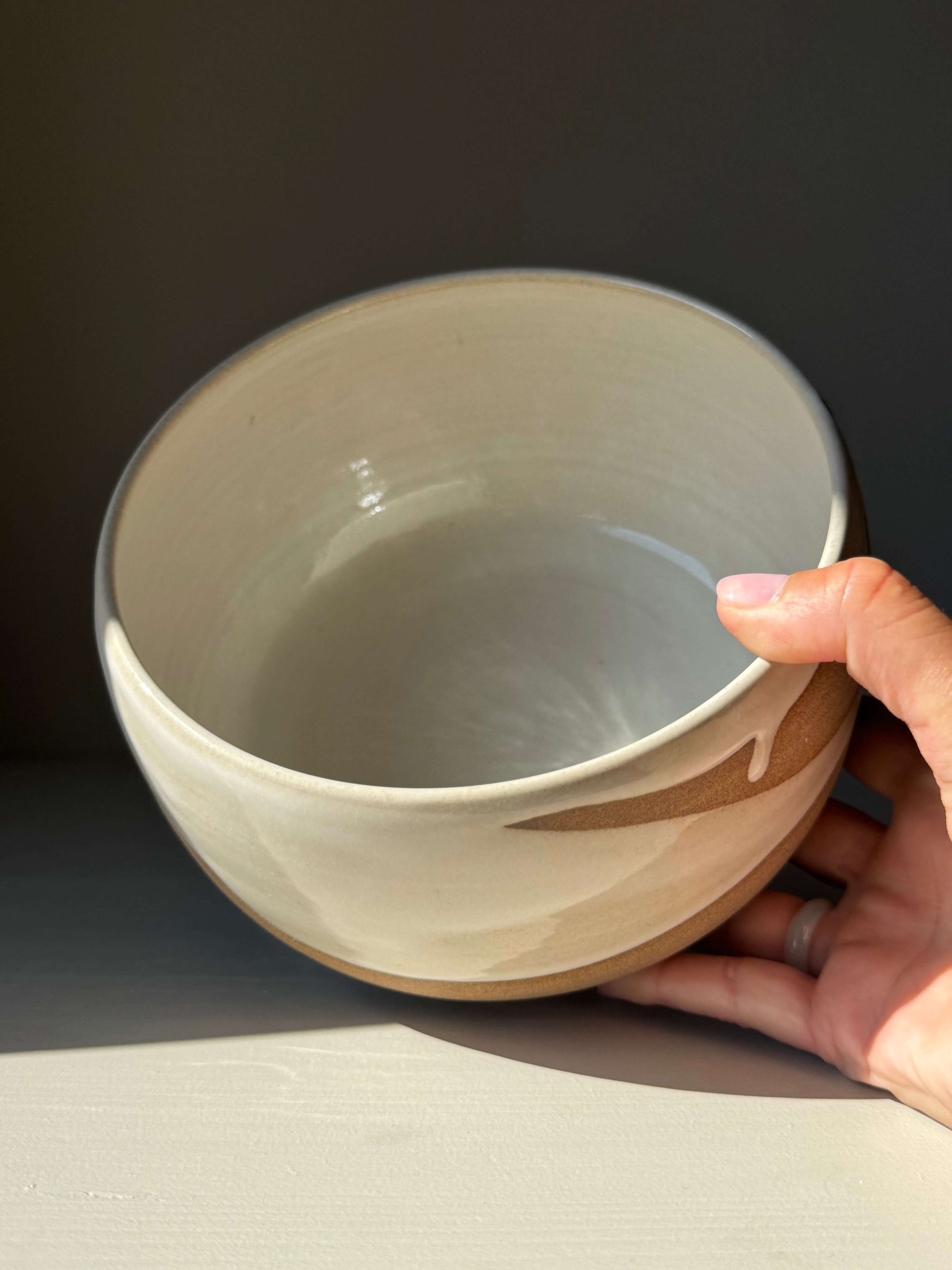 Hand holding Medium Bowl - Yuki #01, a handmade ceramic with glossy white glaze and toffee clay showing soft curves and natural texture.