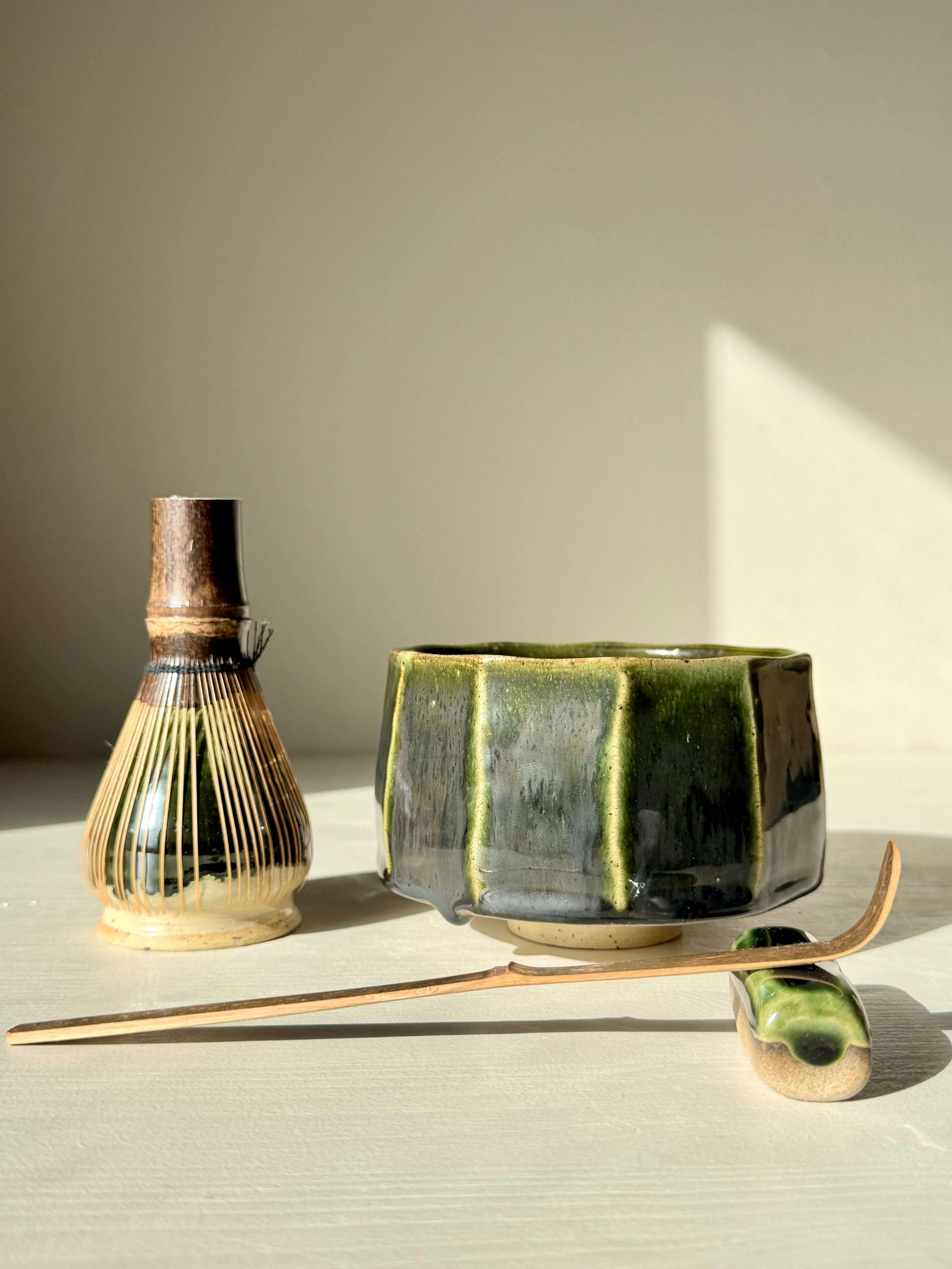 Handmade ceramic Faceted Matcha Bowl - Hinoki Series #01 with deep green glaze, next to a bamboo whisk and spoon.