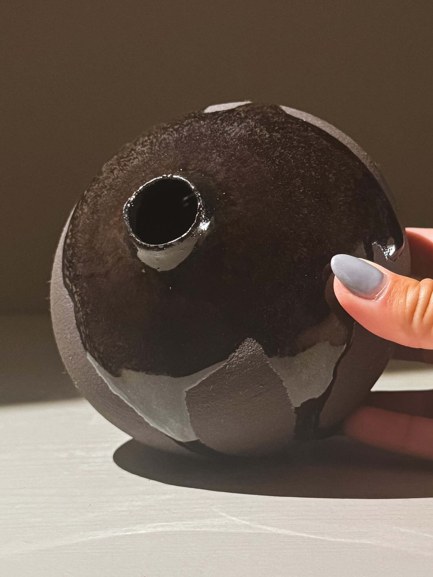 Close-up of Orb Vase – Kuro Black #02, showcasing unique glaze drips and rounded form, held by hand.