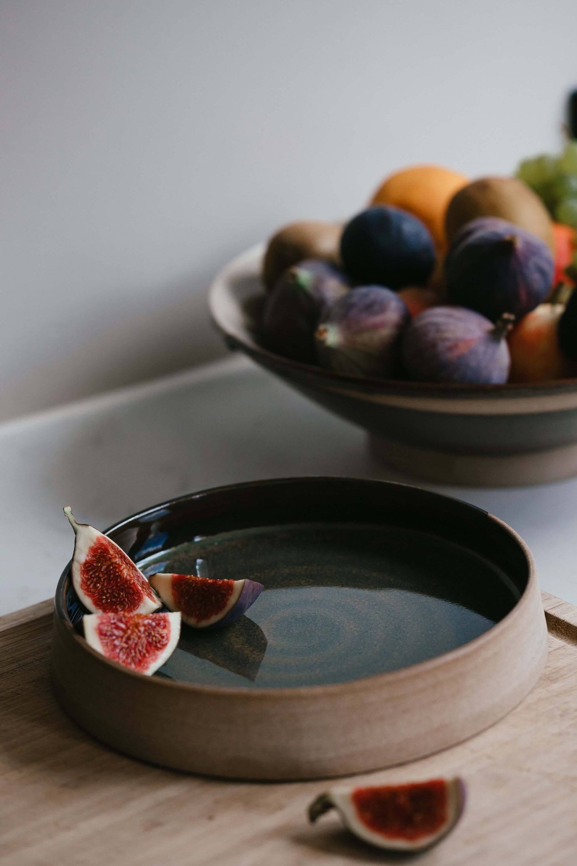 Handmade ceramic Plate – Inyo Series with tenmoku glaze, figs on top, low open form with raw clay edge, showcasing elegance and versatility.