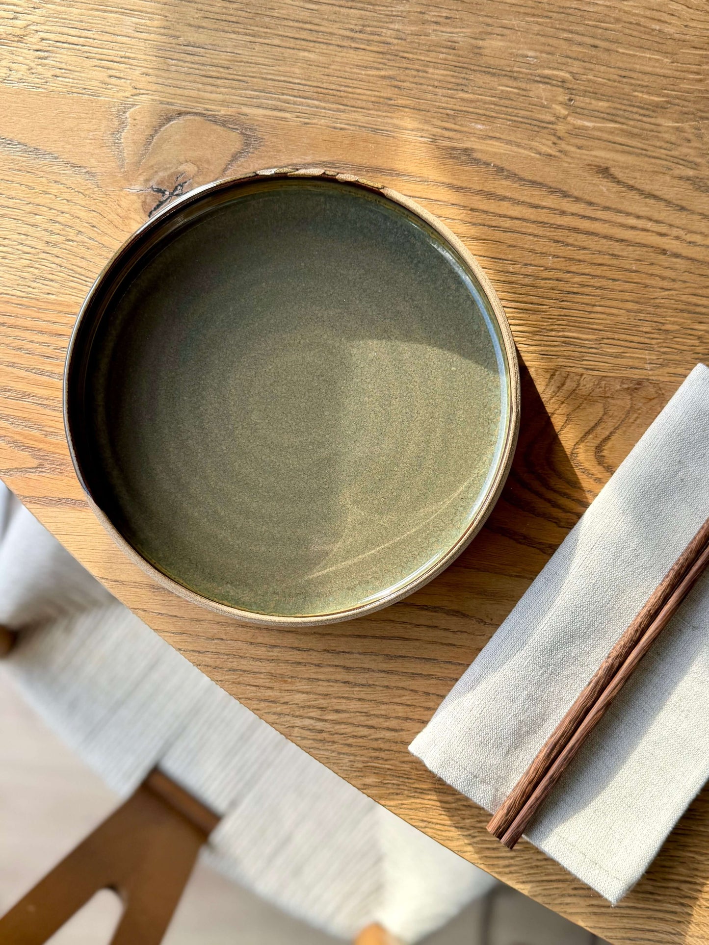 Handmade ceramic Plate – Inyo Series with glossy tenmoku glaze on a wooden table with chopsticks and napkin.