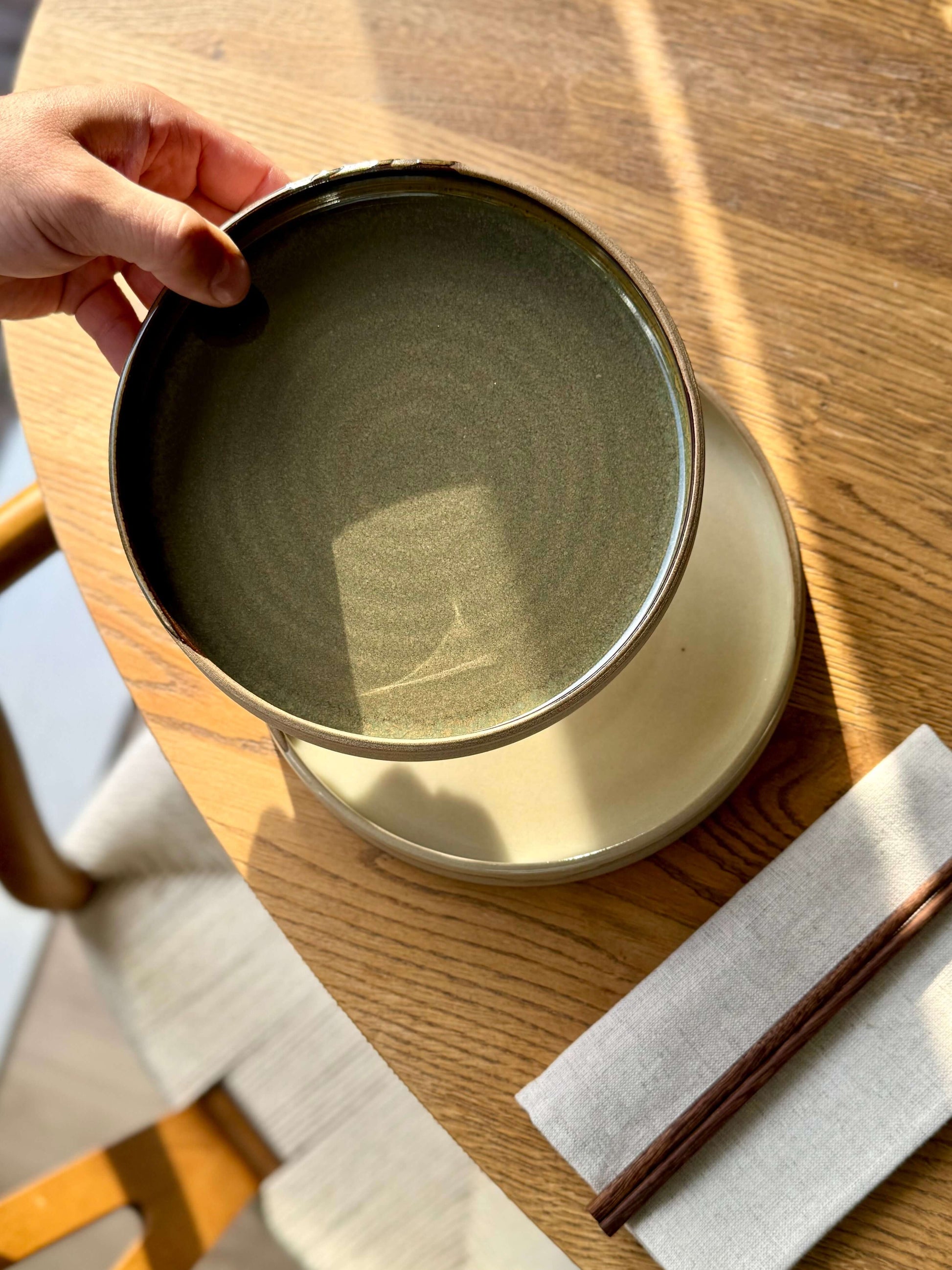 Handmade ceramic Plate – Inyo Series with glossy tenmoku glaze, displaying unique low form with raw edge, placed on wooden table.
