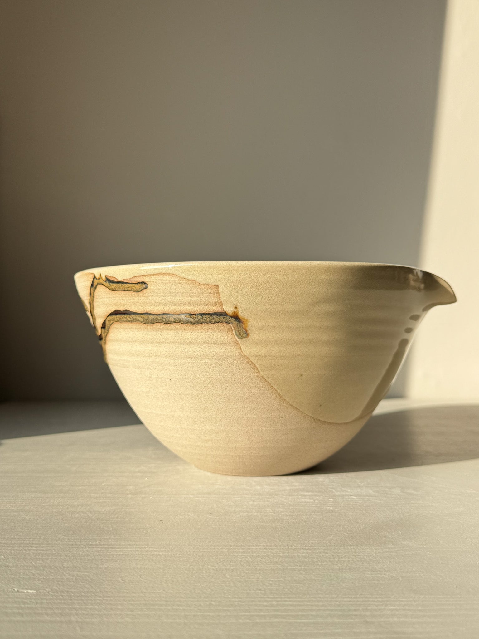 Pouring Bowl – Inyo in natural light, showcasing glossy tenmoku and clear glaze over toffee clay with a spout and spiral lines.