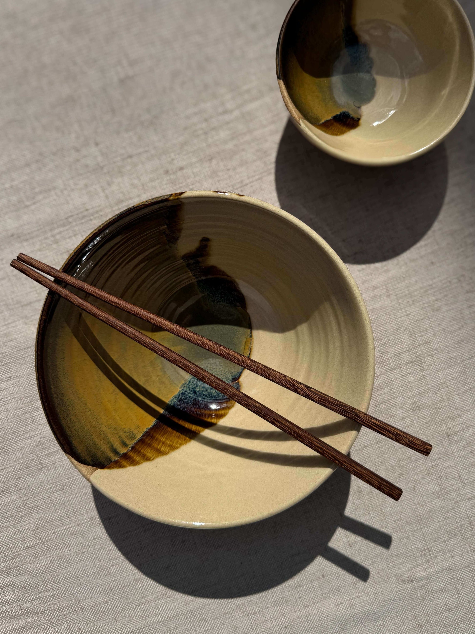 Handmade ceramic Small Bowl - Inyo with a unique tenmoku glaze, showcasing duality in form and color, accompanied by wooden chopsticks.