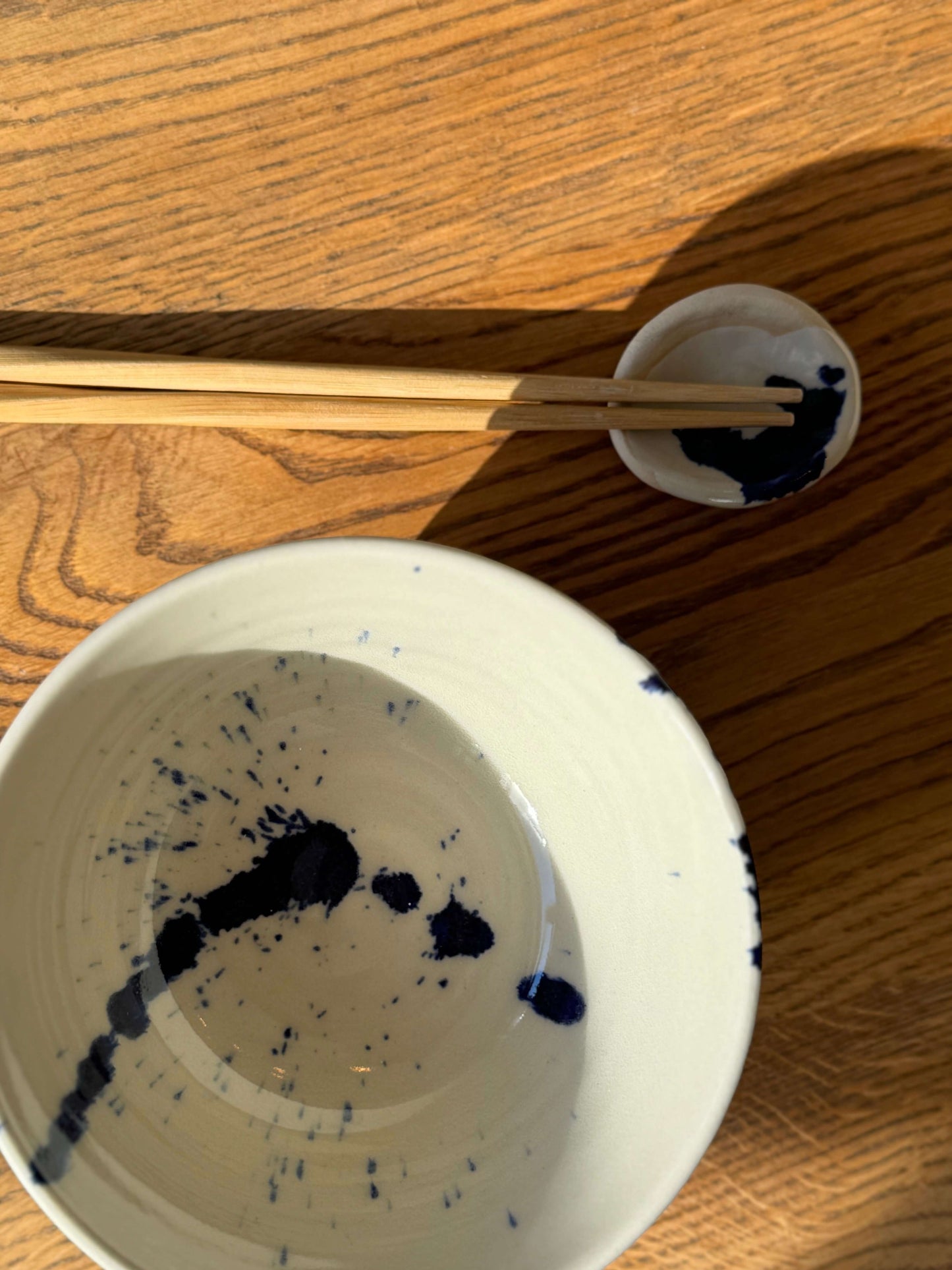 Round Chopstick/Spoon Rest – Gosu in handmade ceramic with cobalt blue splashes beside chopsticks on a wooden table.