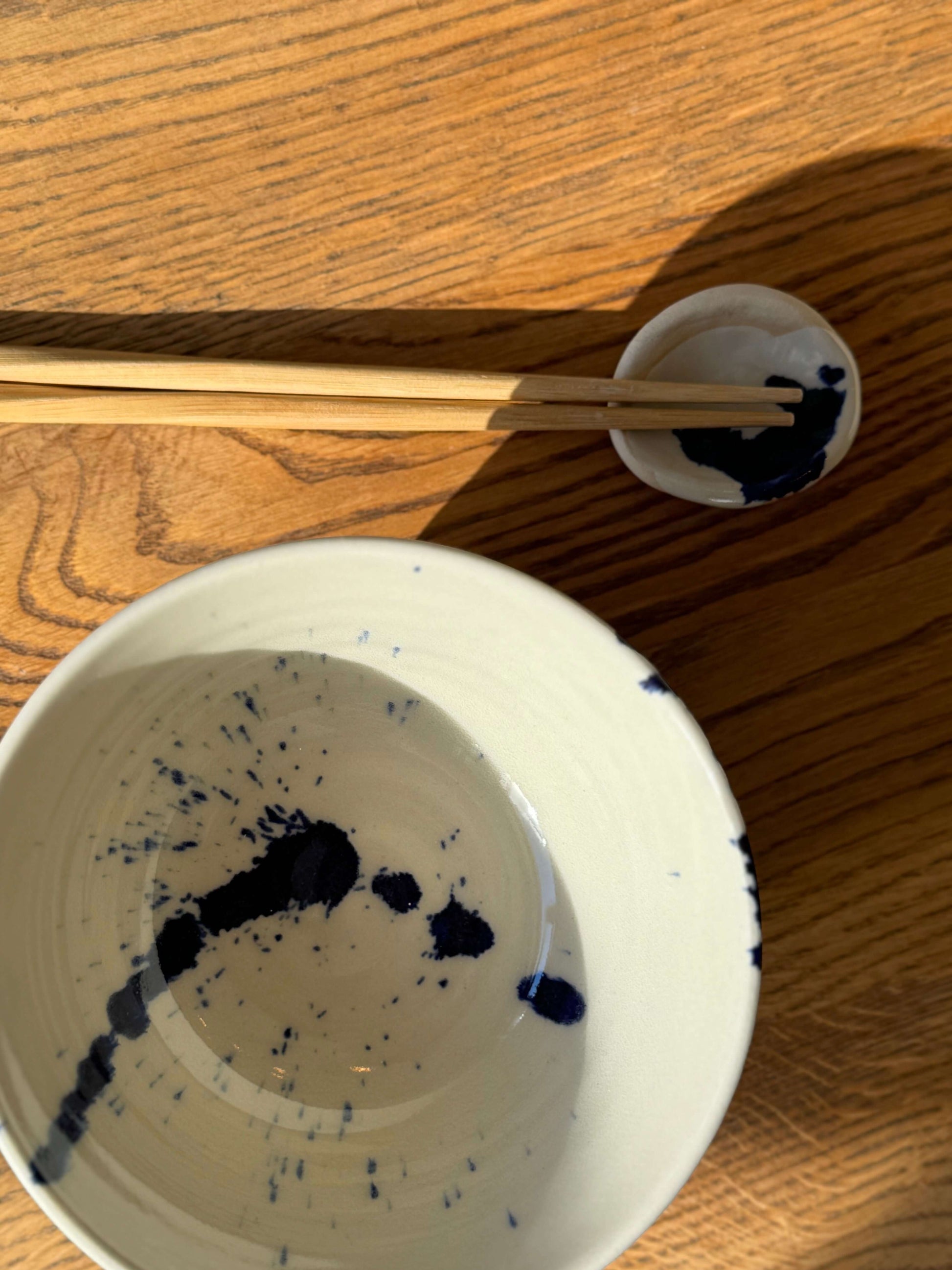 Round Chopstick/Spoon Rest – Gosu in handmade ceramic with cobalt blue splashes beside chopsticks on a wooden table.