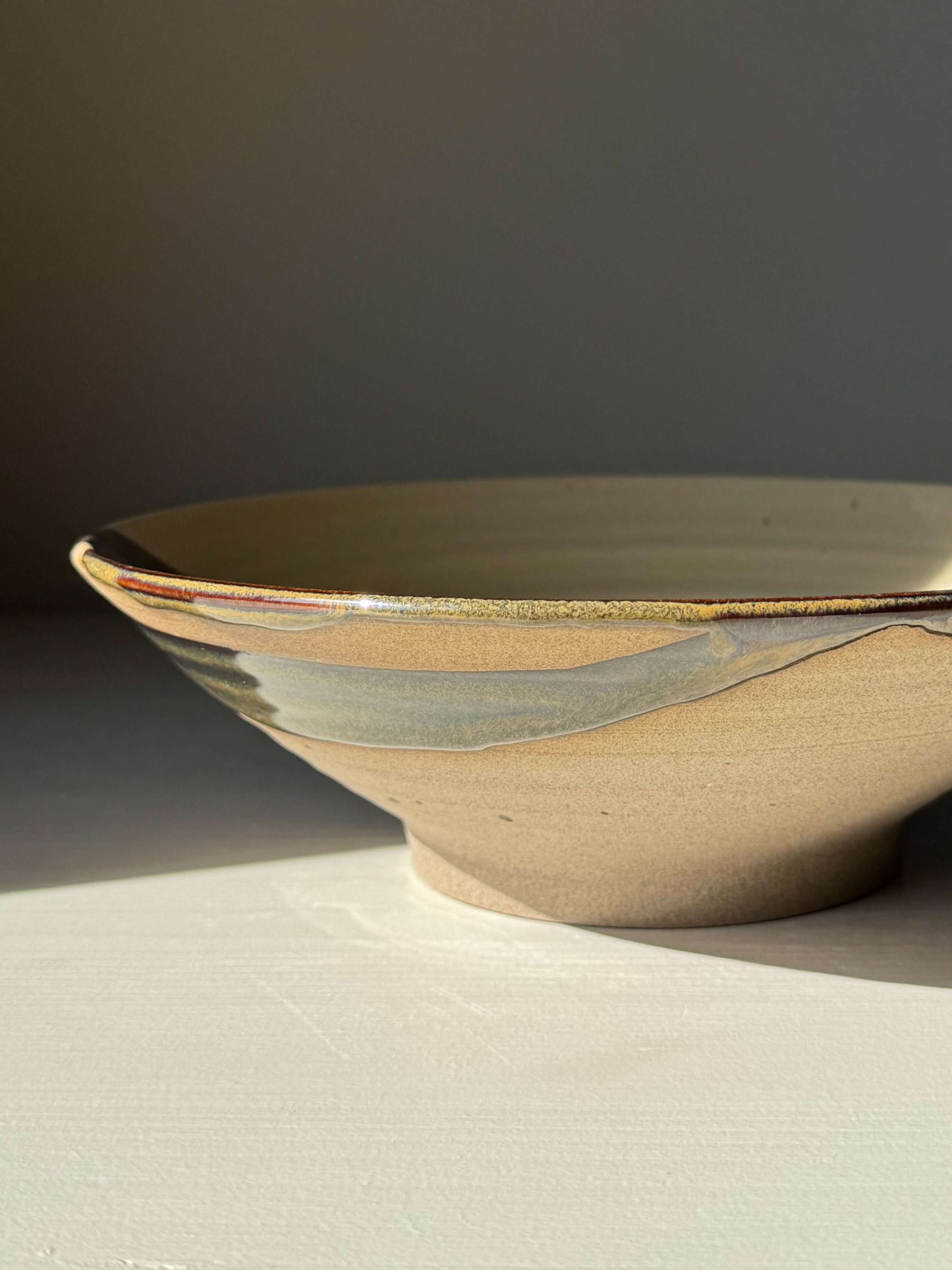 Handmade ceramic Salad/Pasta Plate – Inyo with clear glaze and Tenmoku accents, 23 cm wide, showcasing natural light and dark contrast.