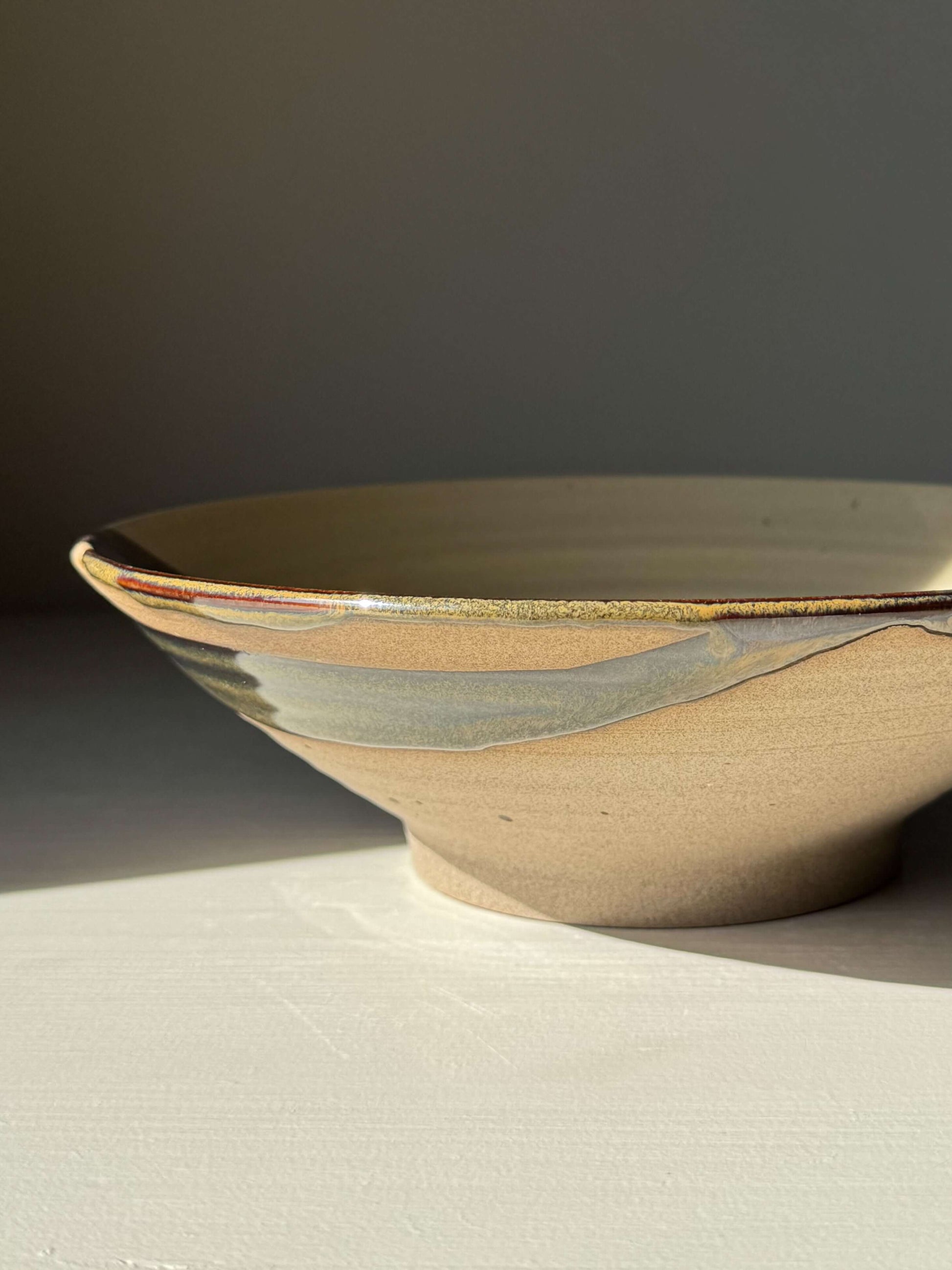 Handmade ceramic Salad/Pasta Plate – Inyo with clear glaze and Tenmoku accents, 23 cm wide, showcasing natural light and dark contrast.