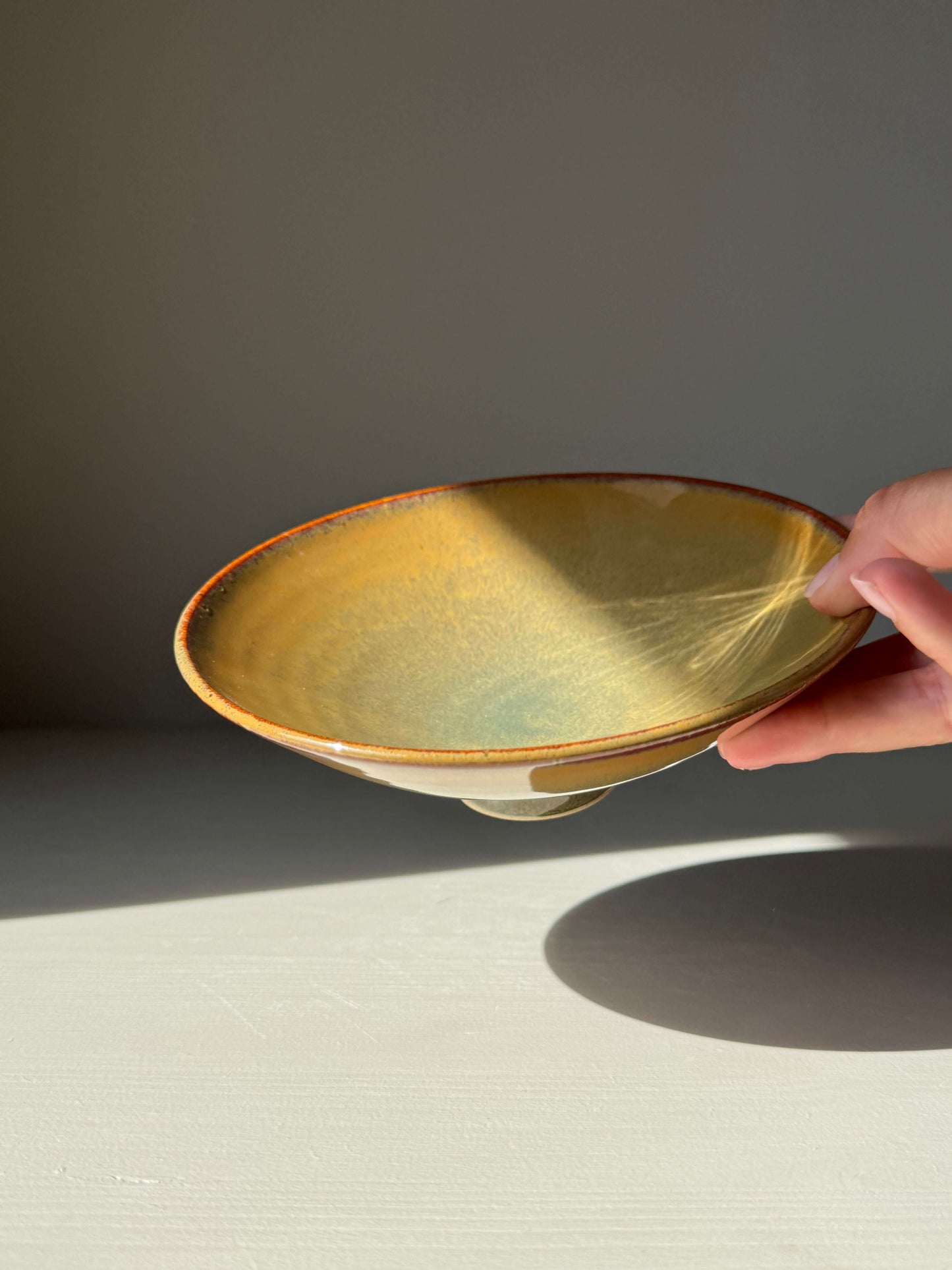 Handmade ceramic Shallow Dish - Tenmoku Glaze with golden amber and warm brown hues, held against a light background.