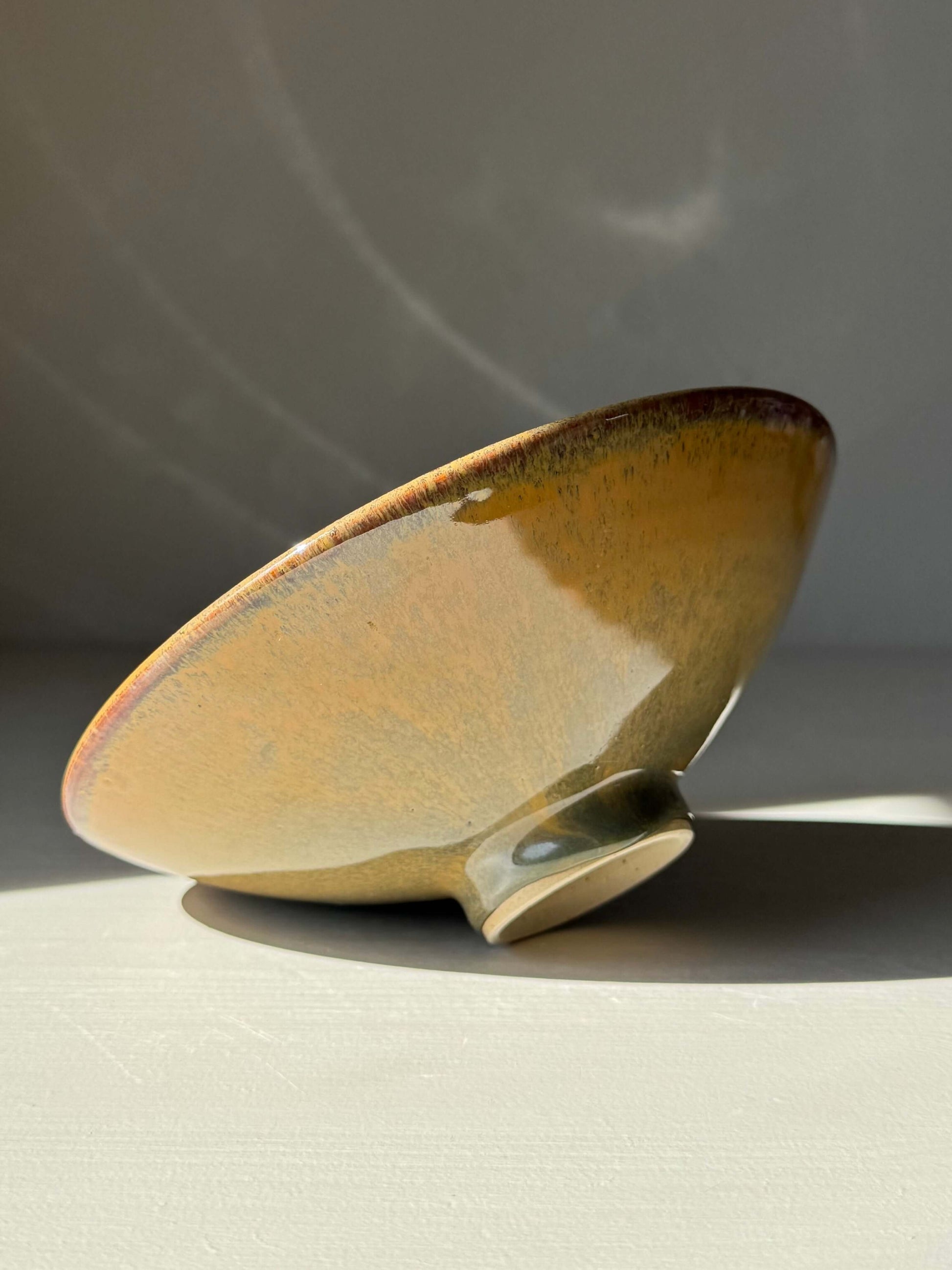 Shallow Dish - Tenmoku Glaze handmade ceramic with amber and brown hues presented on a raised foot, highlighting its unique design.