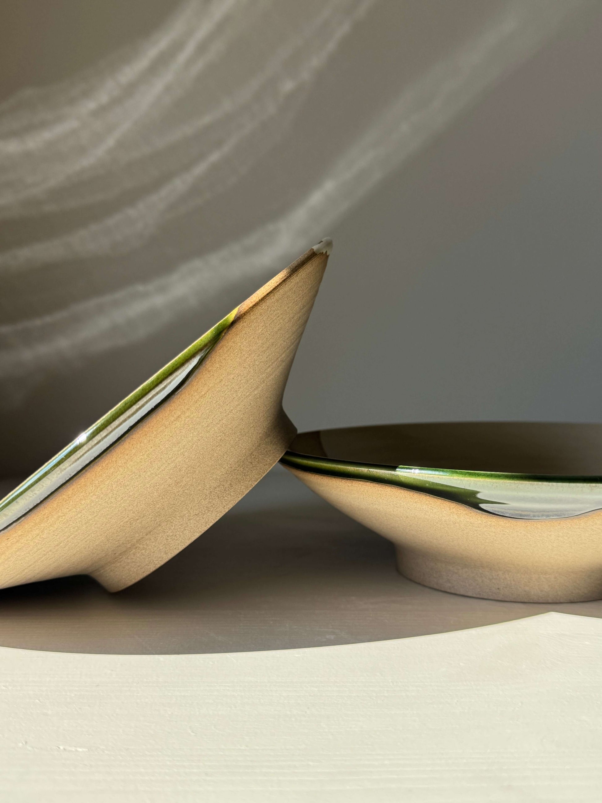 Handmade ceramic Shallow Plate – Mori Series in glossy forest-green finish, side view showing wide, shallow form and raw clay texture.