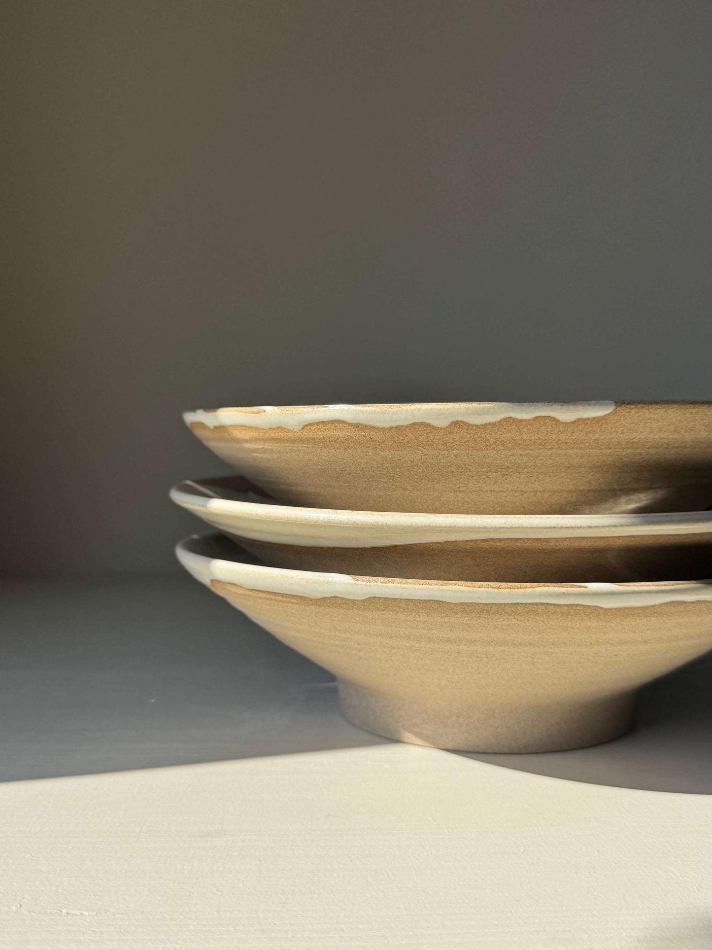 Stack of handmade ceramic Shallow Plate – Yuki Series with white glossy glaze and raw clay exterior.