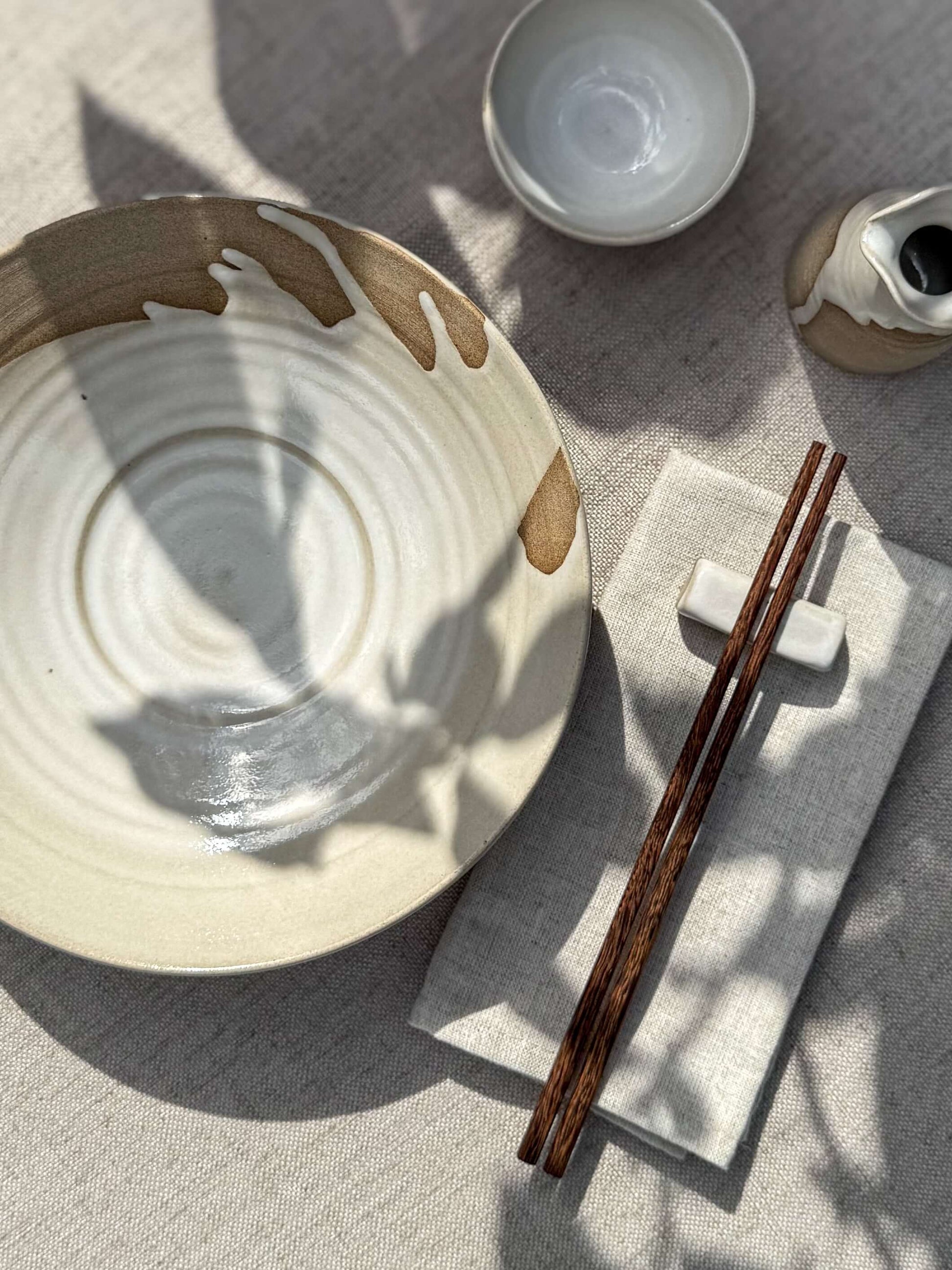 Shallow Plate – Yuki, handmade ceramic with white glaze and raw stoneware accents, displayed with chopsticks on a textured surface.