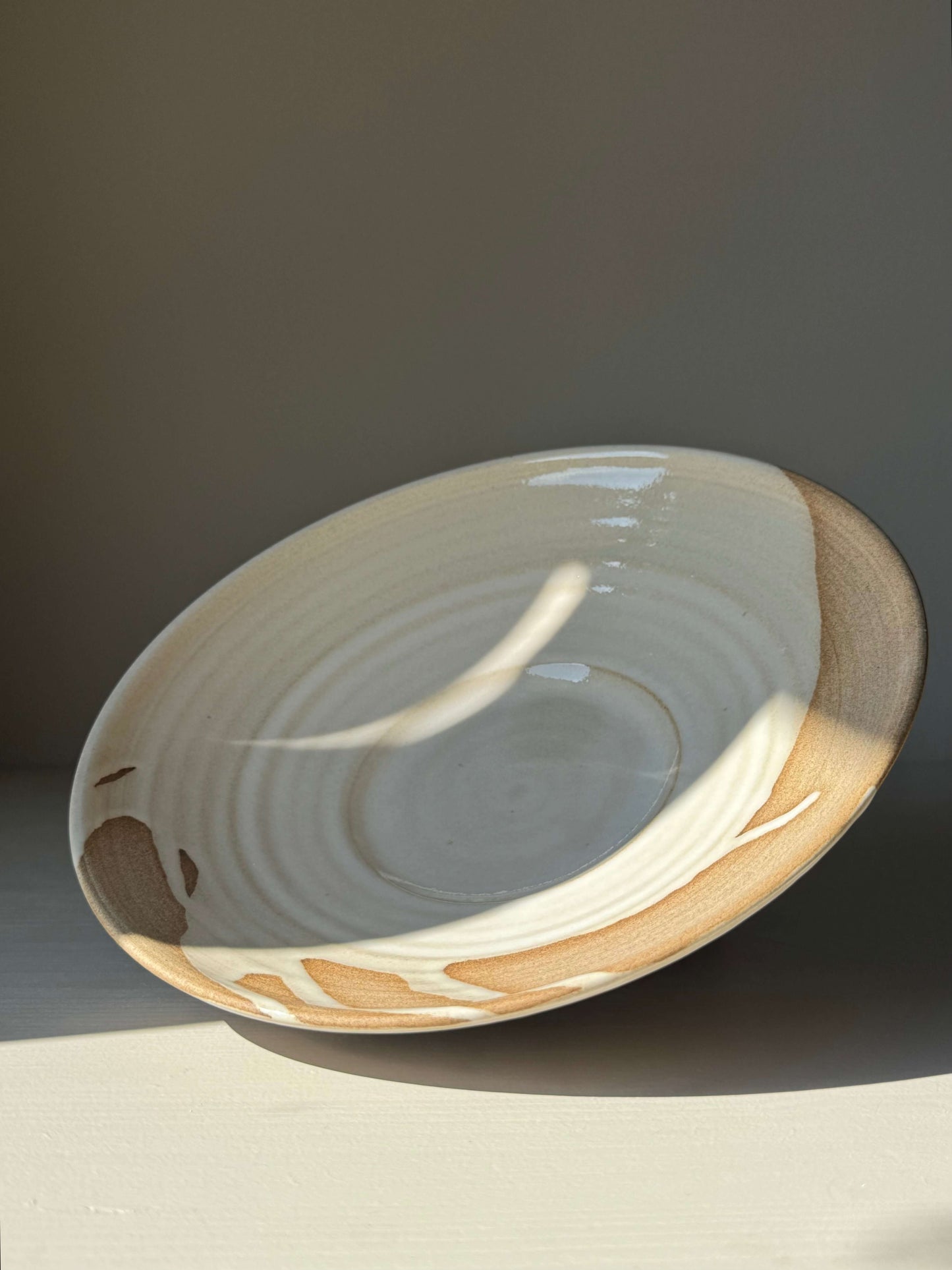 Shallow Plate – Yuki Series handmade ceramic with creamy white glaze and raw stoneware accents in sunlight. Approx. 23 cm diameter.