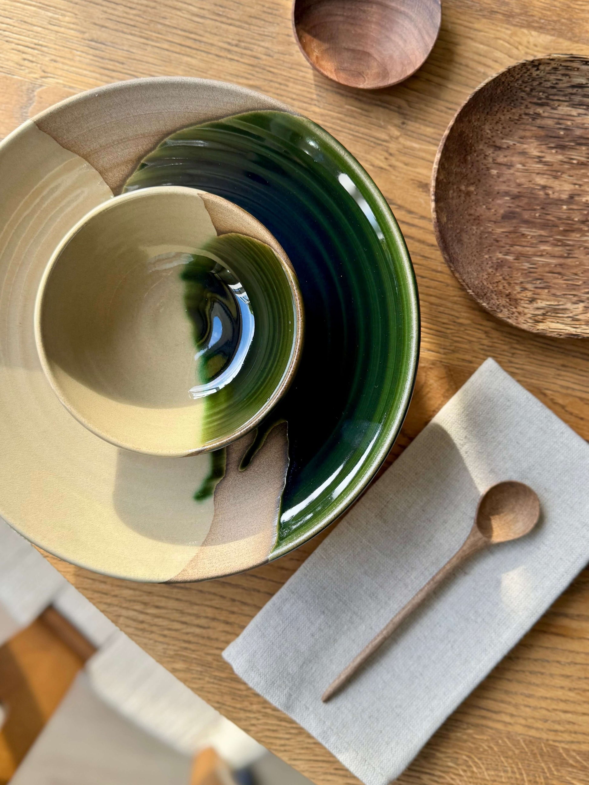 Small Bowl - Mori in green glaze, handmade ceramic on wooden table with spoon and napkin.