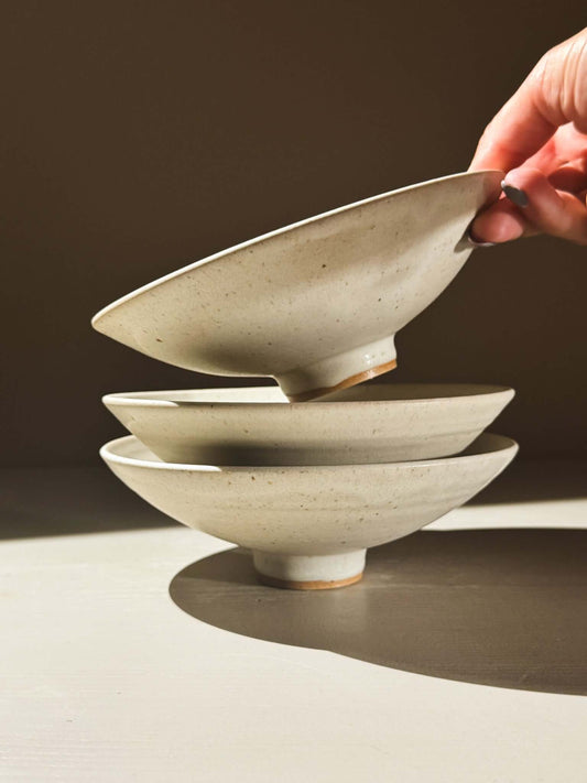 Small Footed Serving Bowl – Eggshell stacked with a hand reaching for the top bowl in soft matte glaze.