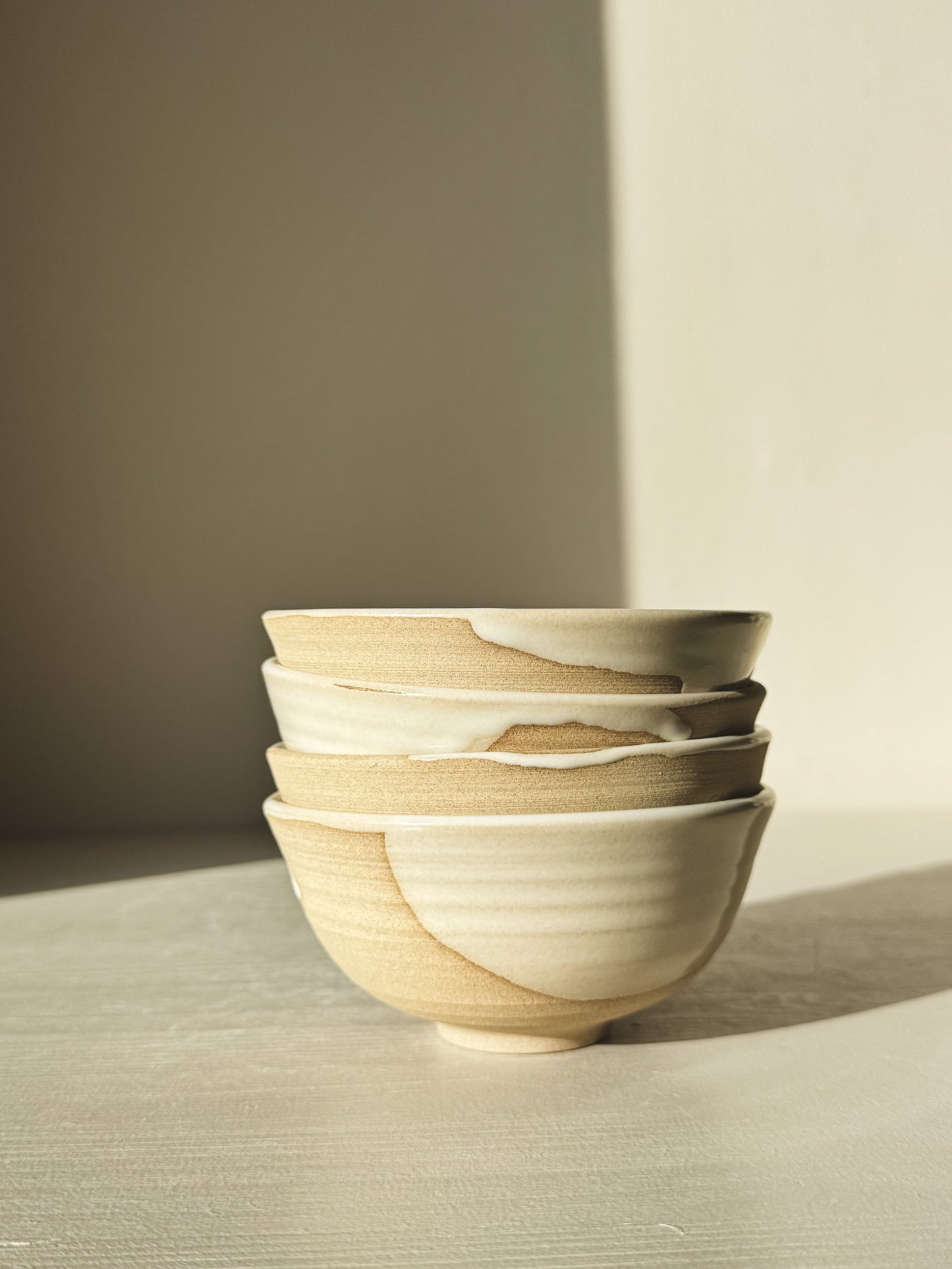 Stack of four Small Bowl - Yuki with white glaze and organic lines displayed in warm natural light.