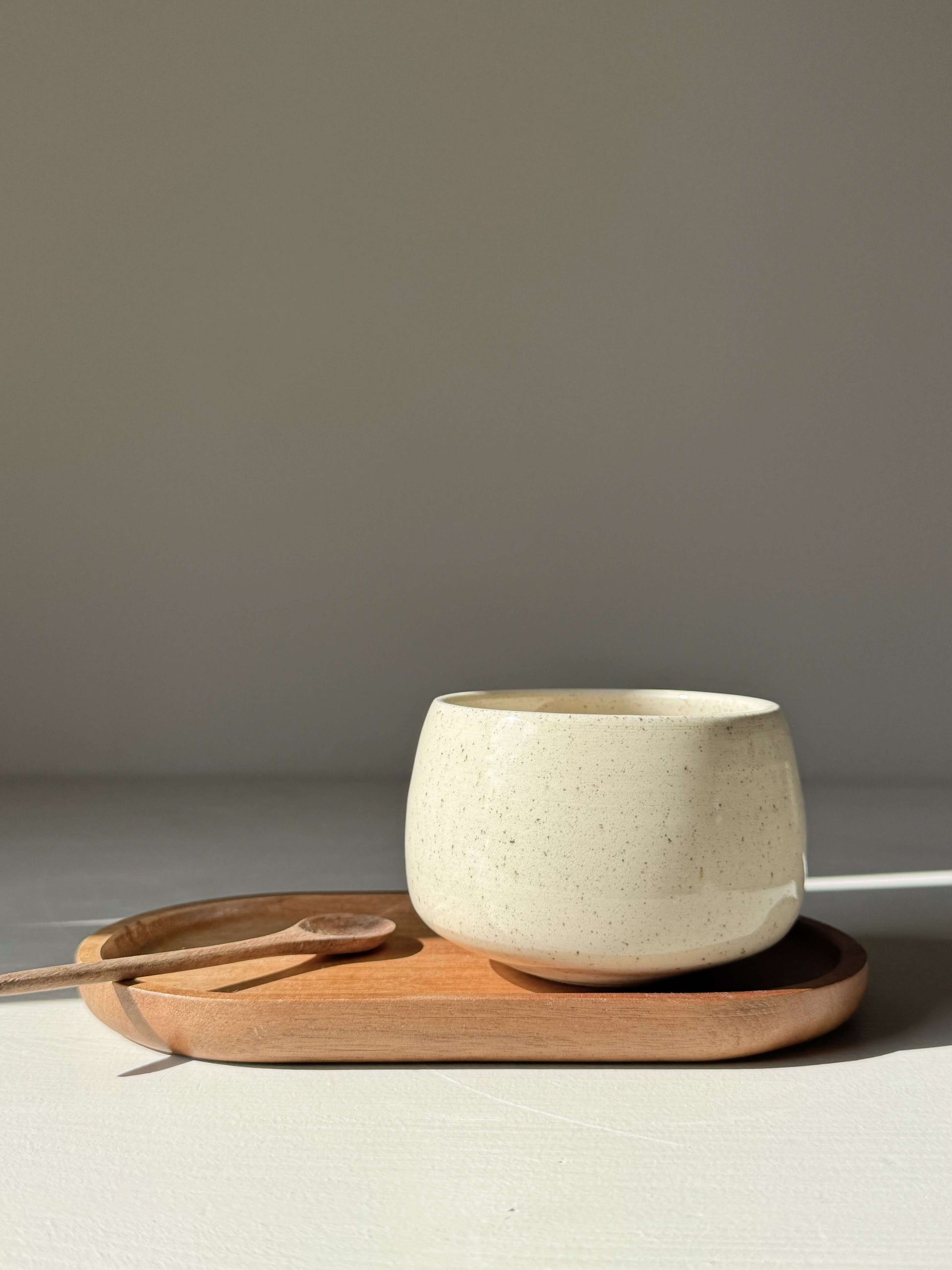 Cups - Speckled Clear Glaze handmade ceramic, soft rounded cup on wooden tray, sunlight highlighting freckled surface, approx. 6.5 cm high.