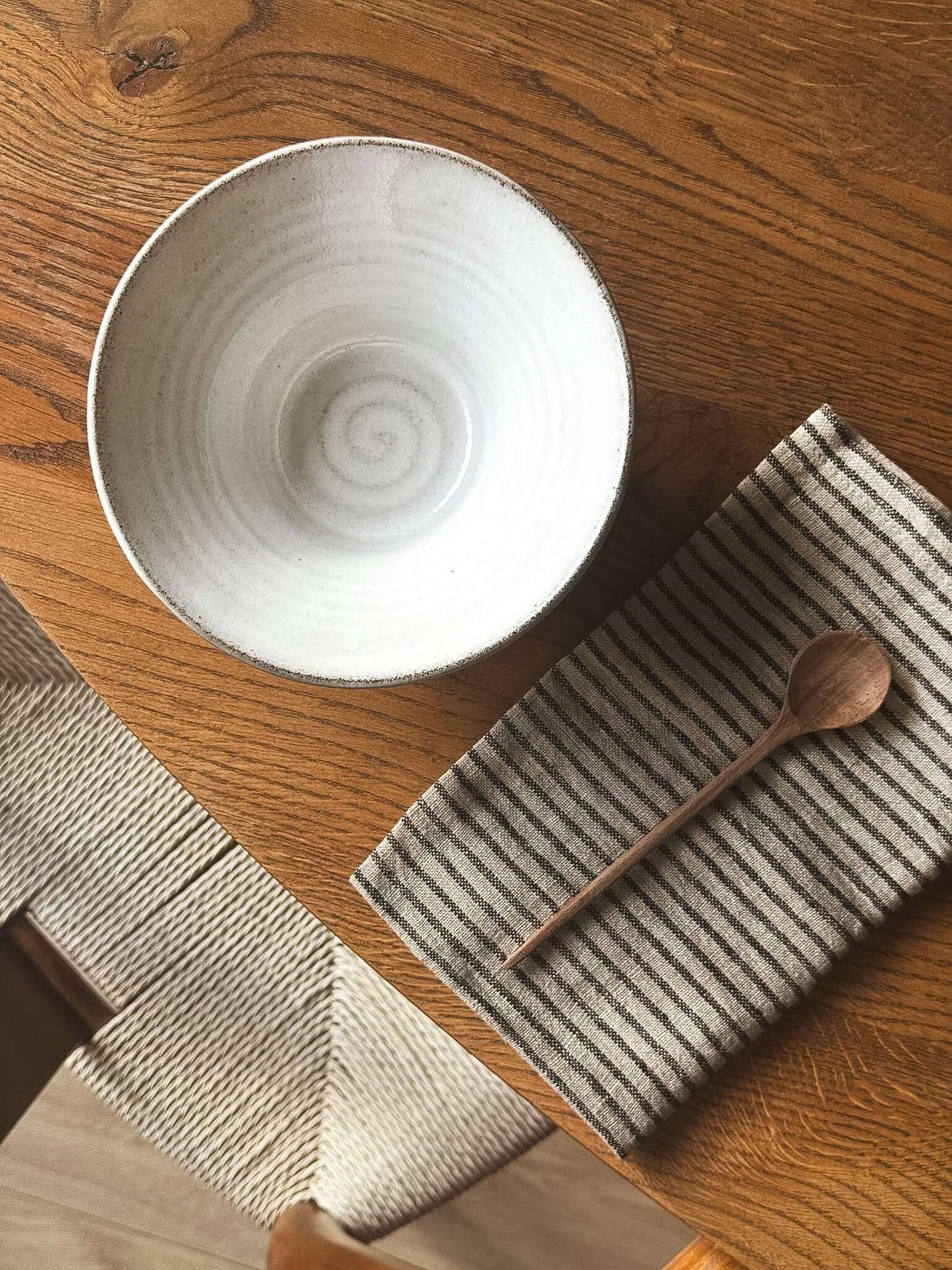 Bowl - Yuki Ash on wooden table with a striped napkin and wooden spoon, showcasing its glossy white glaze.