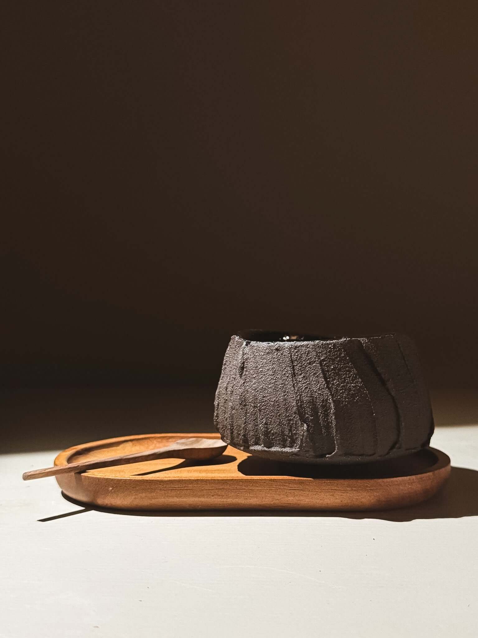 Yunomi Cup - Kuro #03 on wooden tray showcasing textured brown clay and glossy dark glaze.