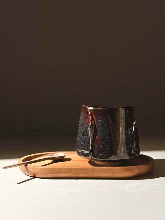 Yunomi Cup - Kuro on wooden tray showcasing glossy black glaze with hints of blue and burgundy, highlighting handmade ceramics pottery.