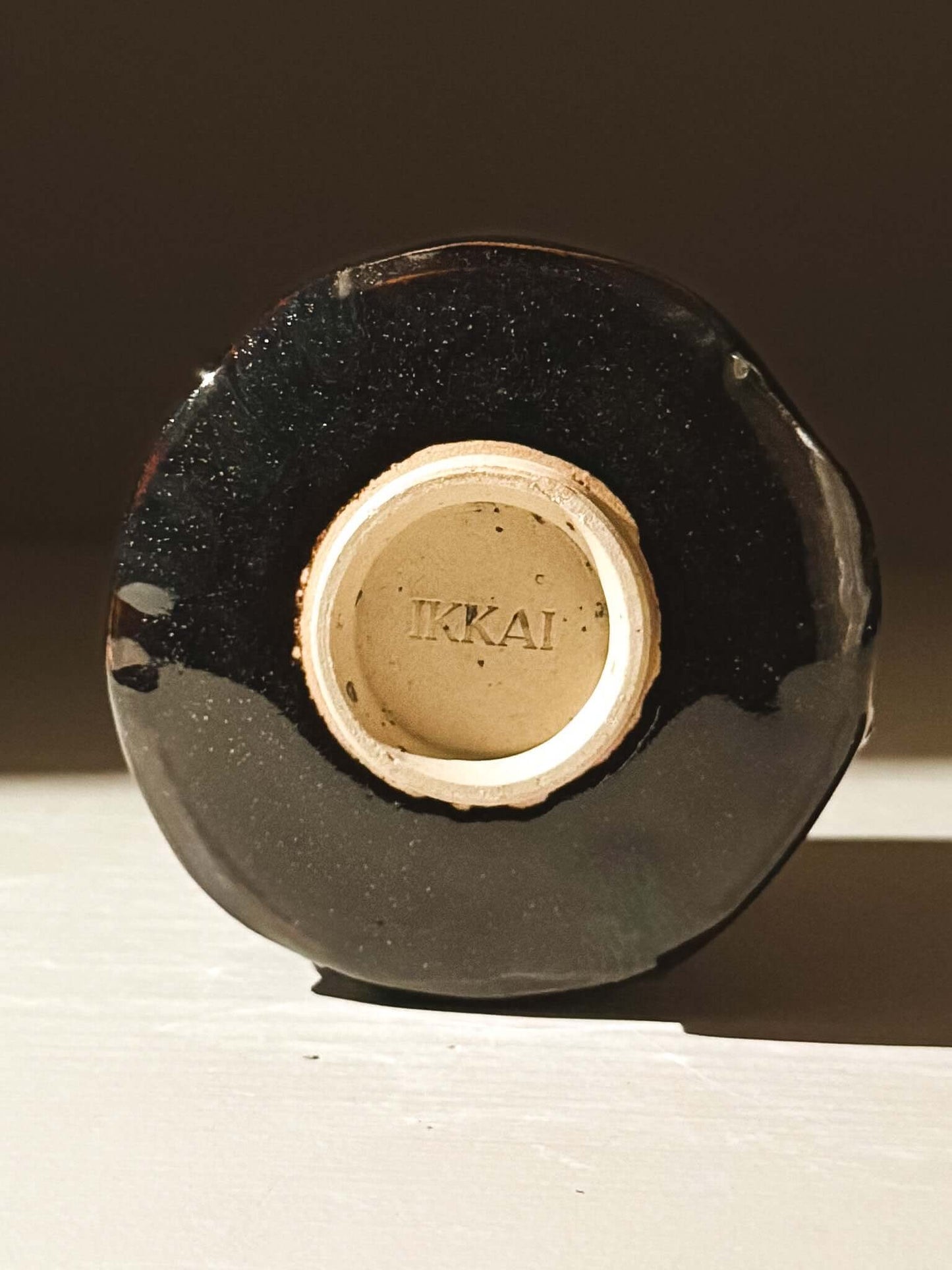 Bottom view of the Yunomi Cup - Kuro, showcasing the handmade craftsmanship and signature mark with glossy black Kuro glaze.