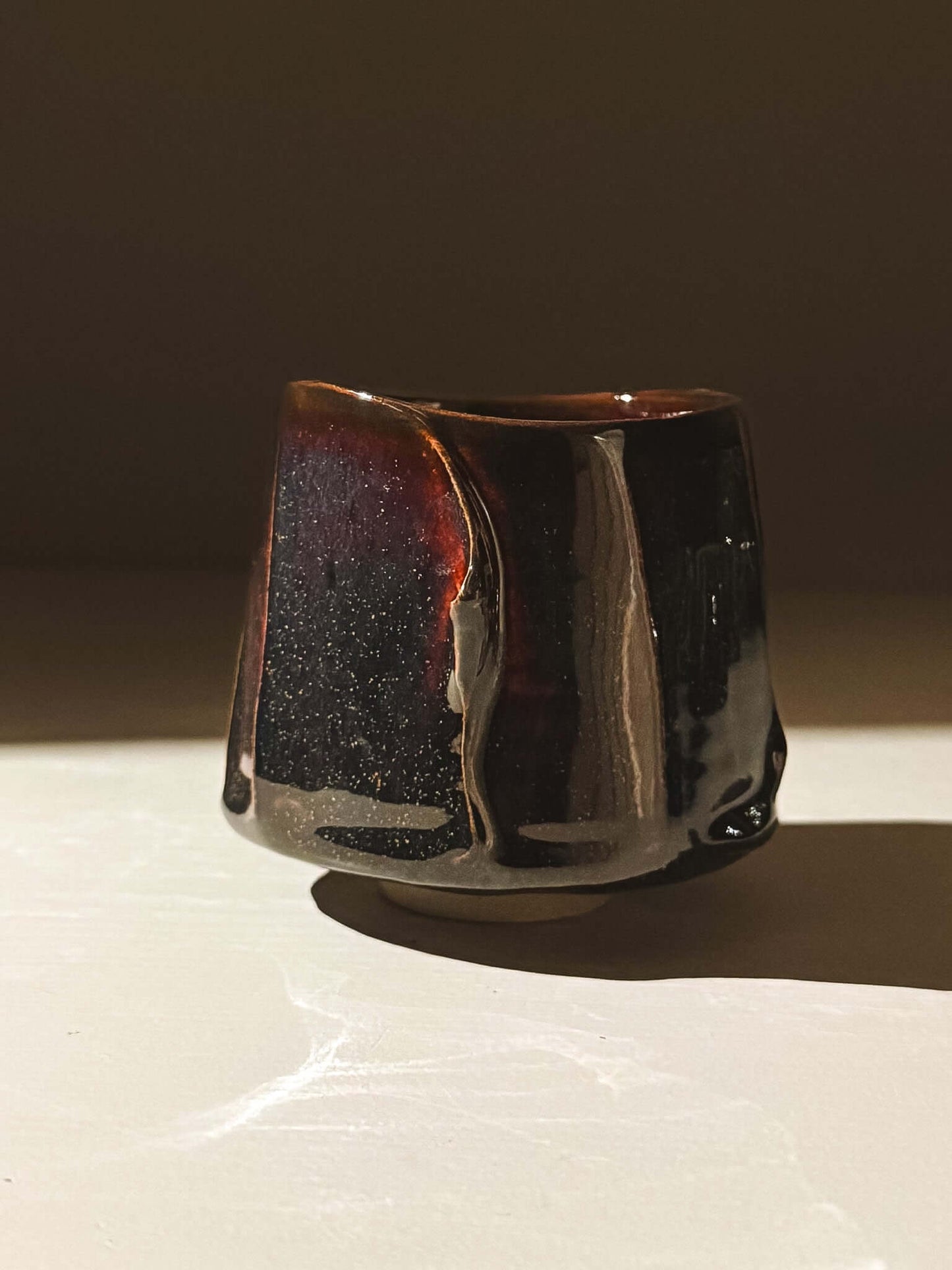 Yunomi Cup - Kuro handmade with glossy black glaze showcasing deep blue, burgundy, and red hues, revealing depth in sunlight.