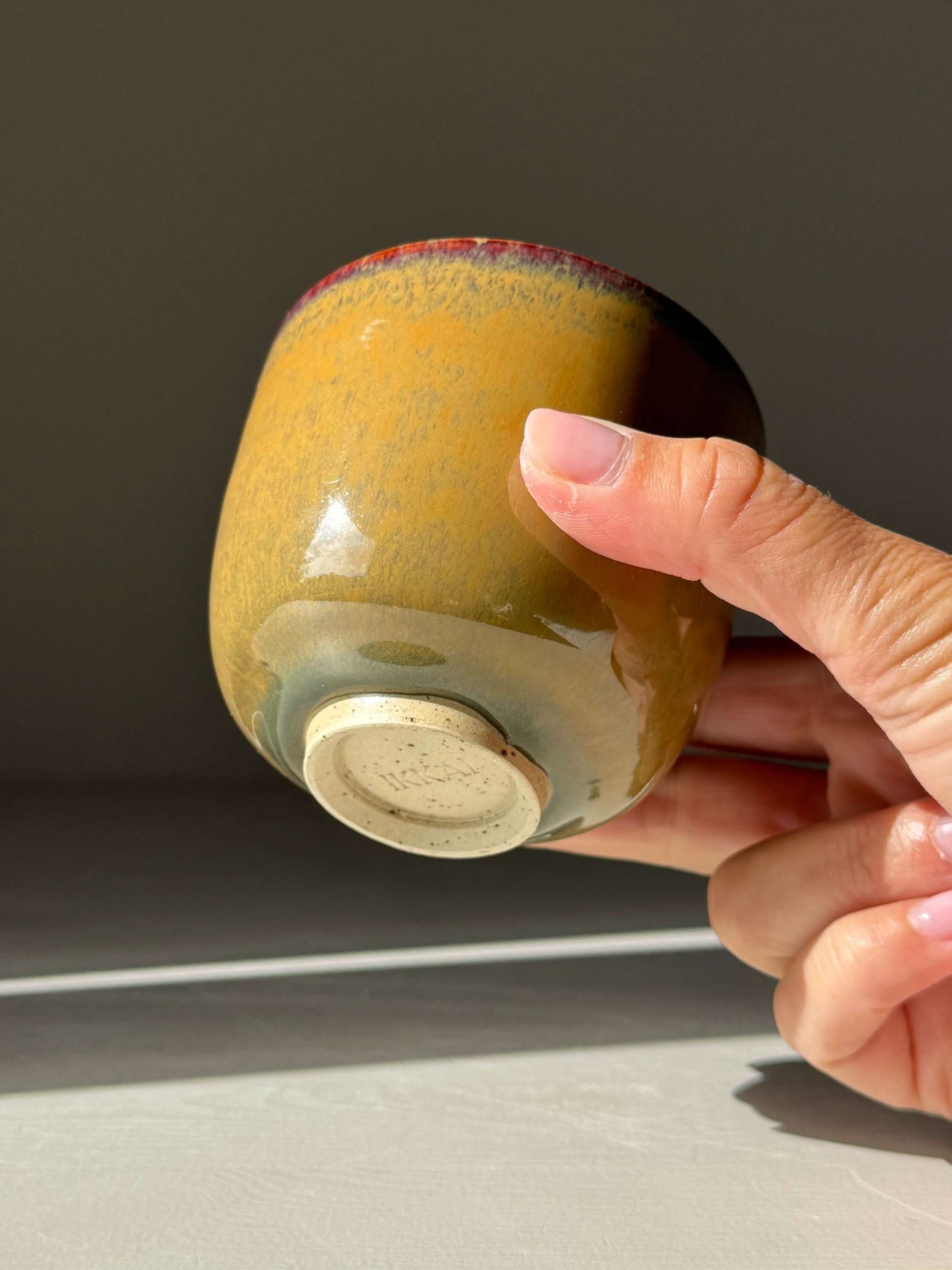 Hand holding handmade ceramic Yunomi Cups - Tenmoku Glaze with warm amber tones under sunlight.