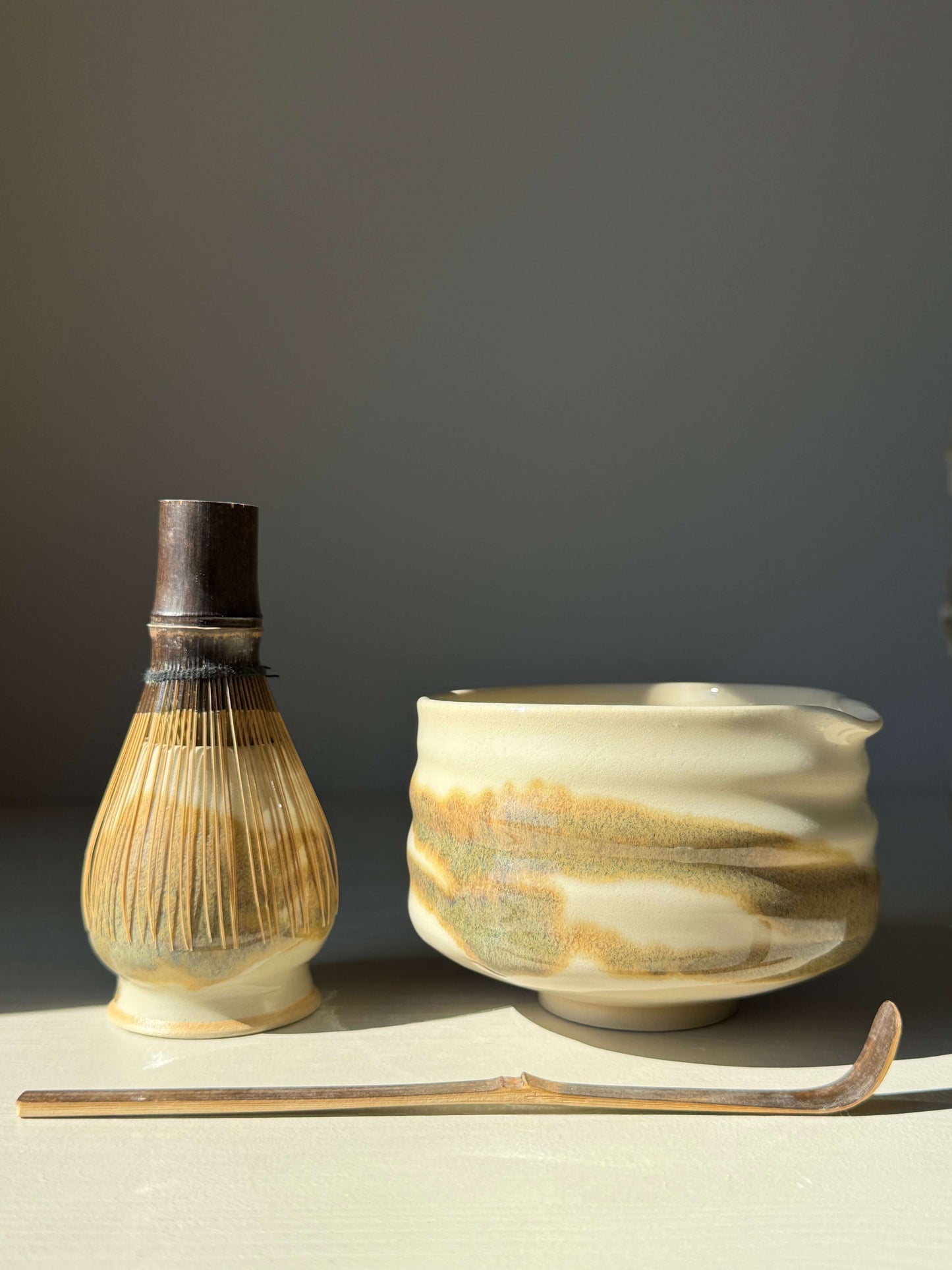 Handmade matcha bowl with spout, clear glaze and tenmoku splashes, accompanied by a traditional bamboo whisk and chashaku spoon.