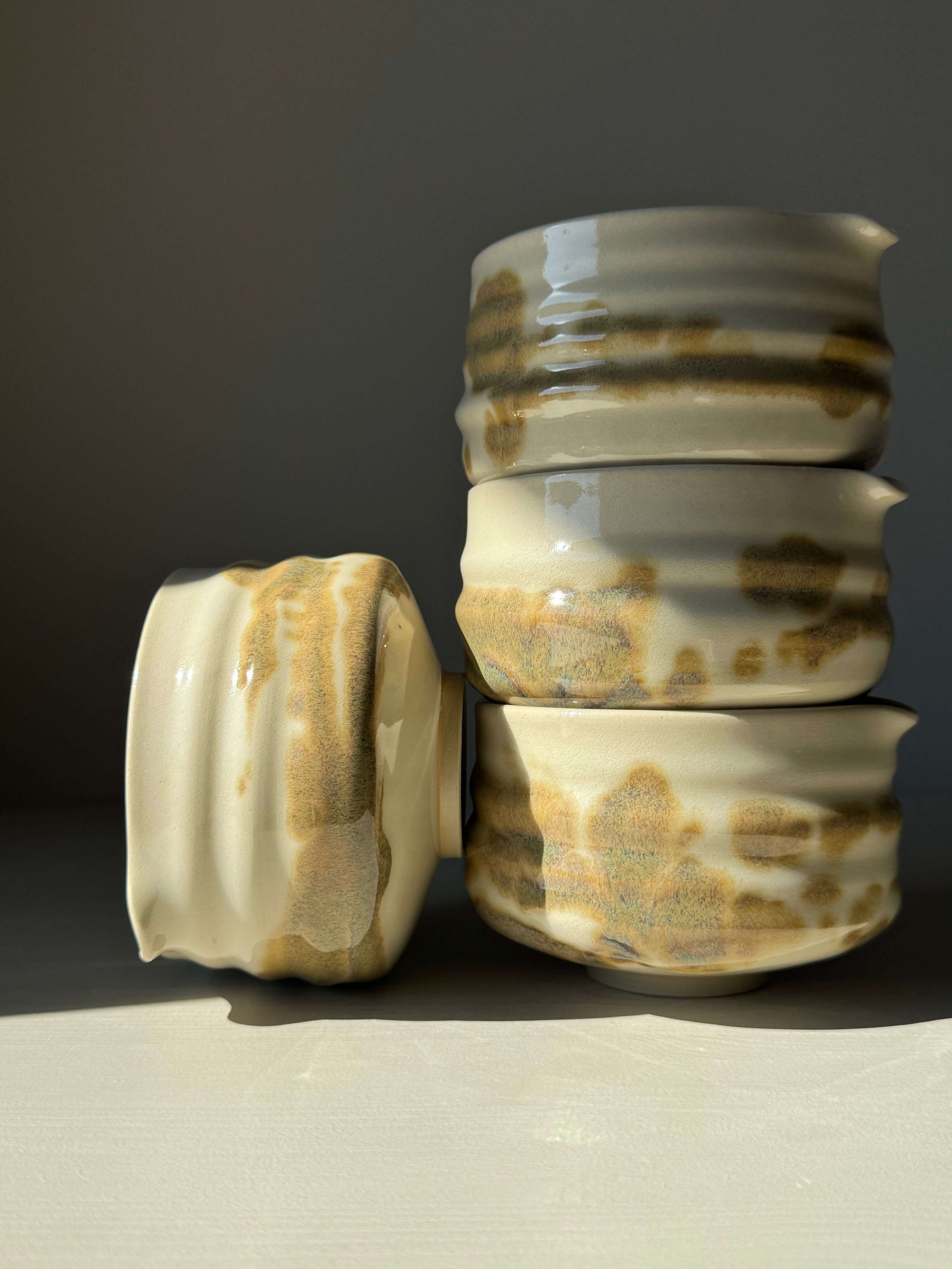 Stack of handmade matcha bowls with clear glaze and tenmoku splashes, featuring soft spouts and unique grooves.