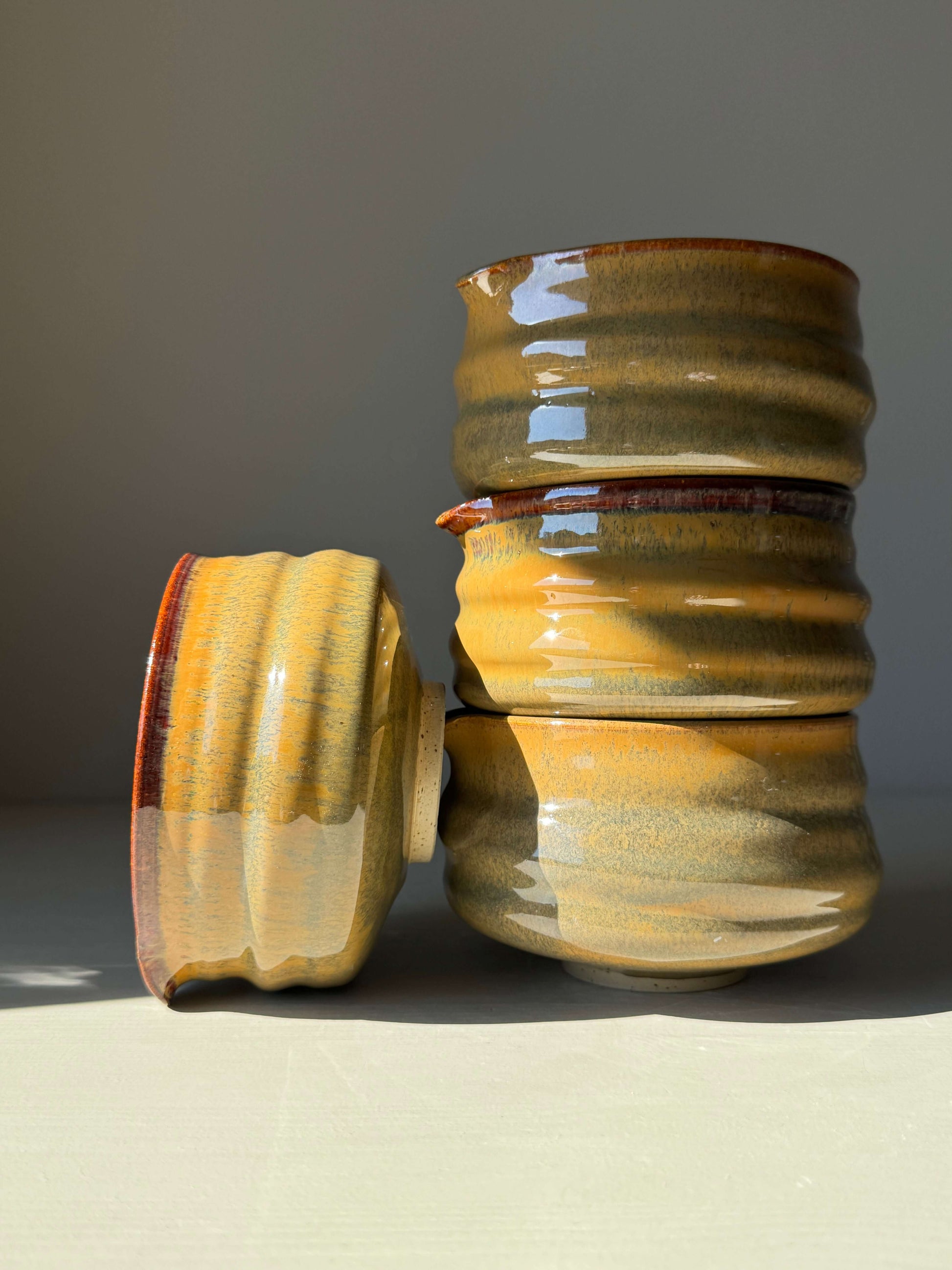 Stack of matcha bowls with spouts in tenmoku glaze, displaying rich brown and soft green hues under sunlight.