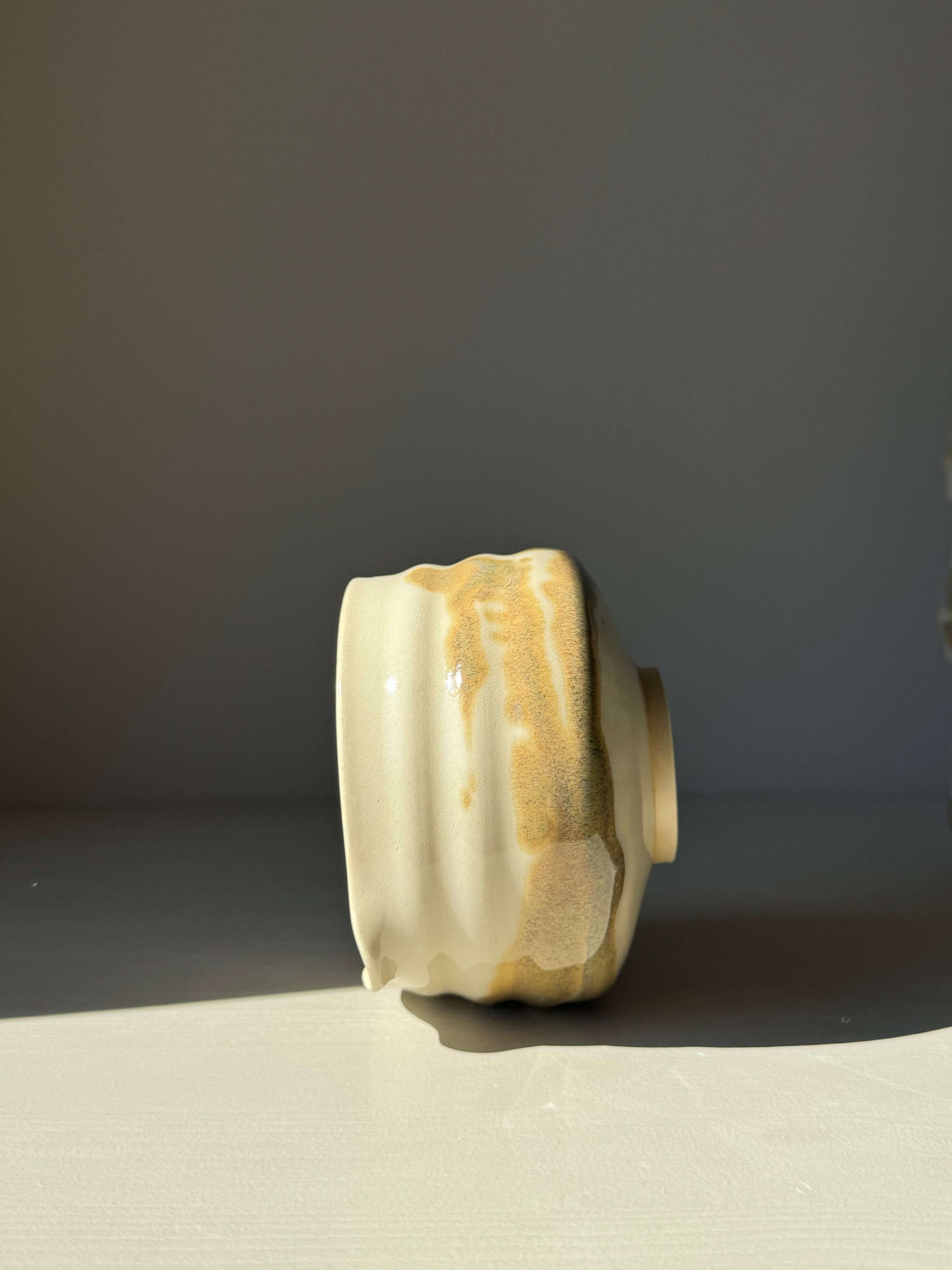 Side view of a handcrafted matcha bowl with clear glaze and tenmoku splashes, showcasing unique grooves and earthy tones.