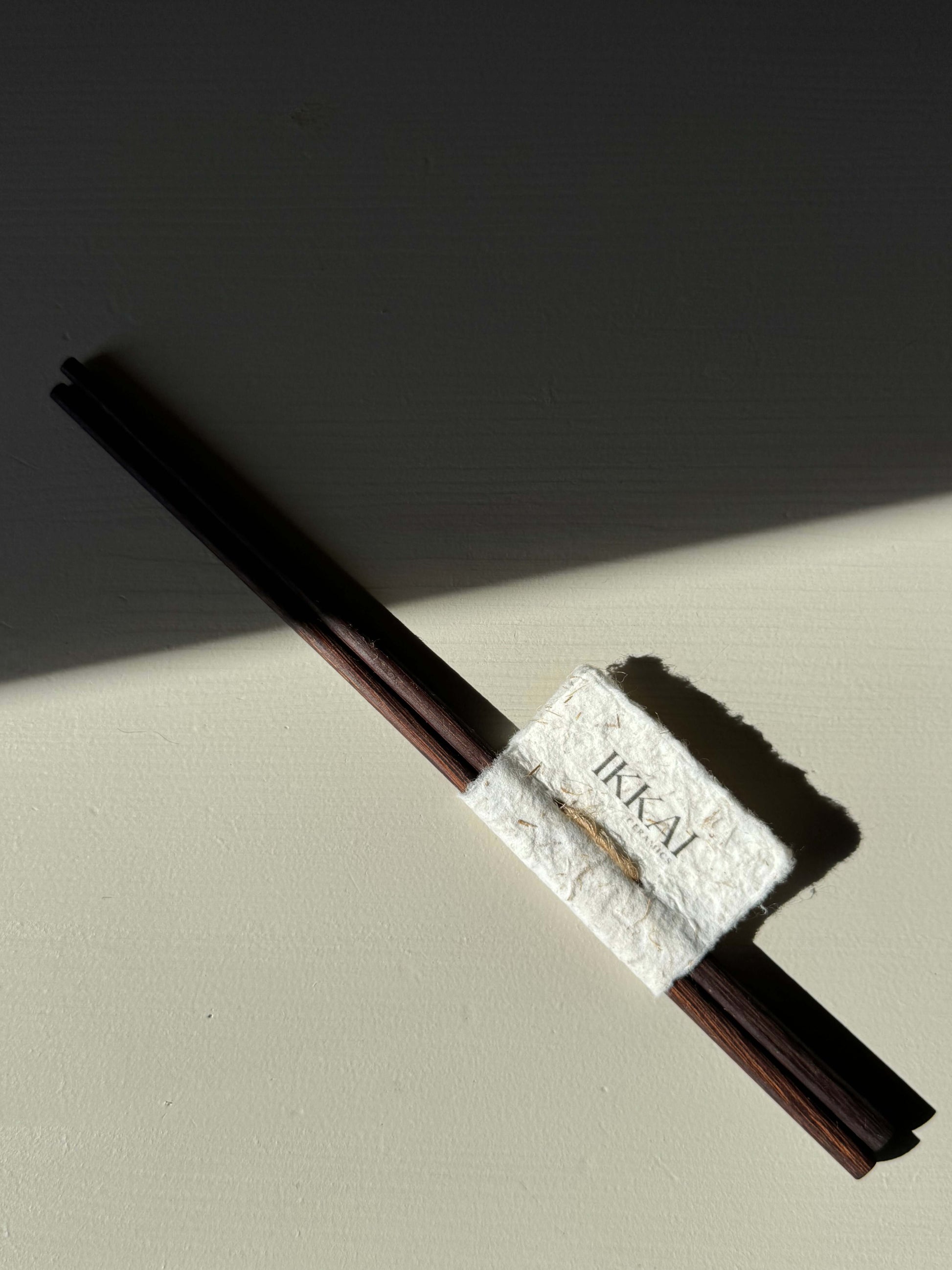 Close-up of Wooden Chopsticks on a light background, wrapped with a handmade ceramic textured band, casting a shadow.