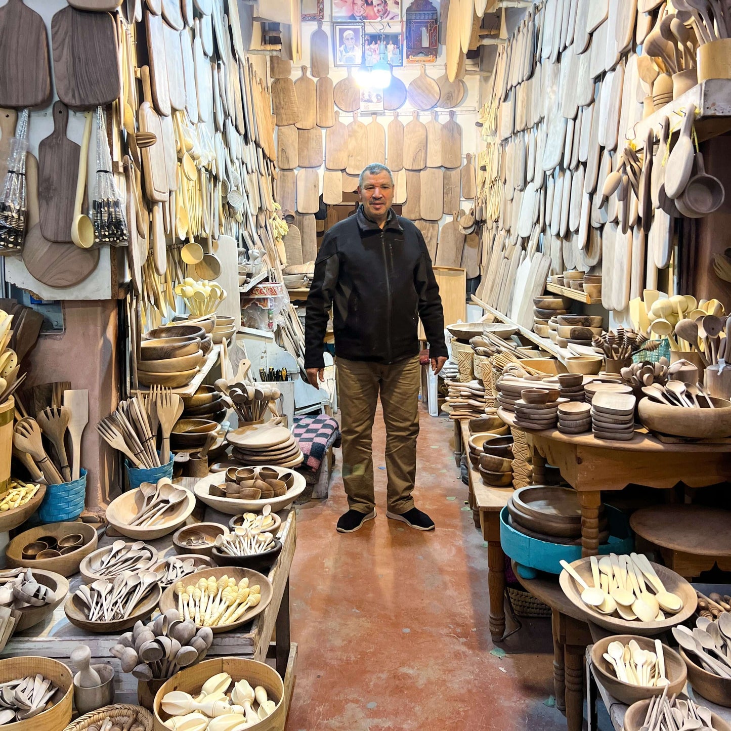 Artisan standing in a shop filled with Medium Walnut Wooden Spoons and handmade ceramic kitchen items in the Medina, Marrakech.