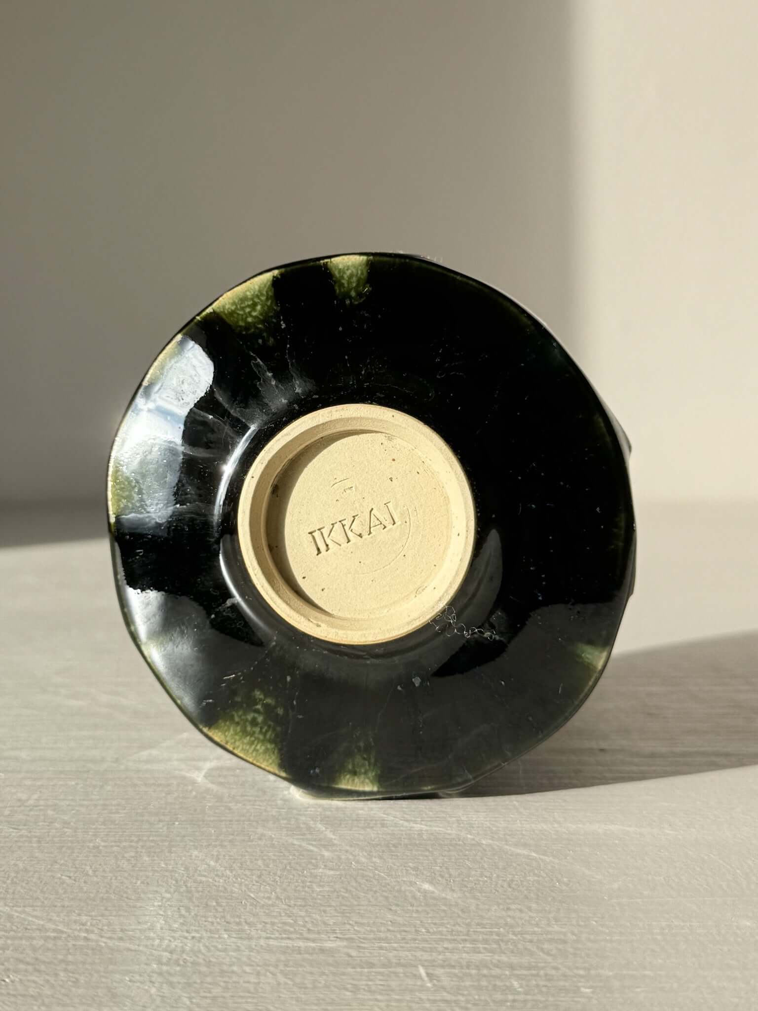 Bottom view of the Yunomi Cup - Hinoki #28 with deep green glaze and textured design, showcasing the maker's mark 'IKKAI'.