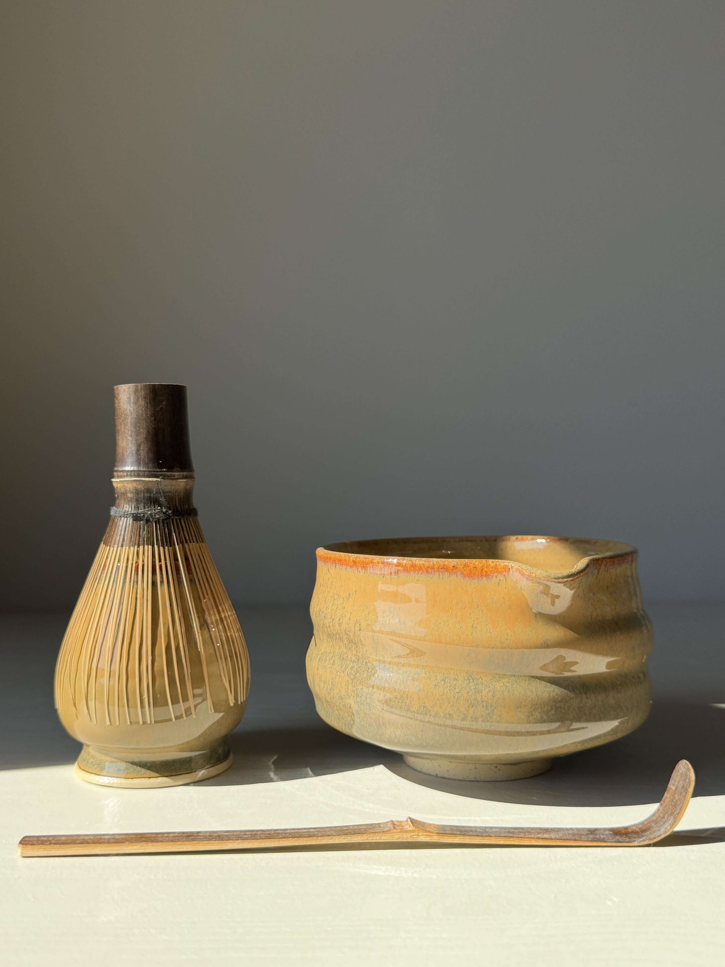 Alt Tag: Hand-thrown matcha bowl with spout and tenmoku glaze, paired with a bamboo whisk and spoon, under soft natural light.