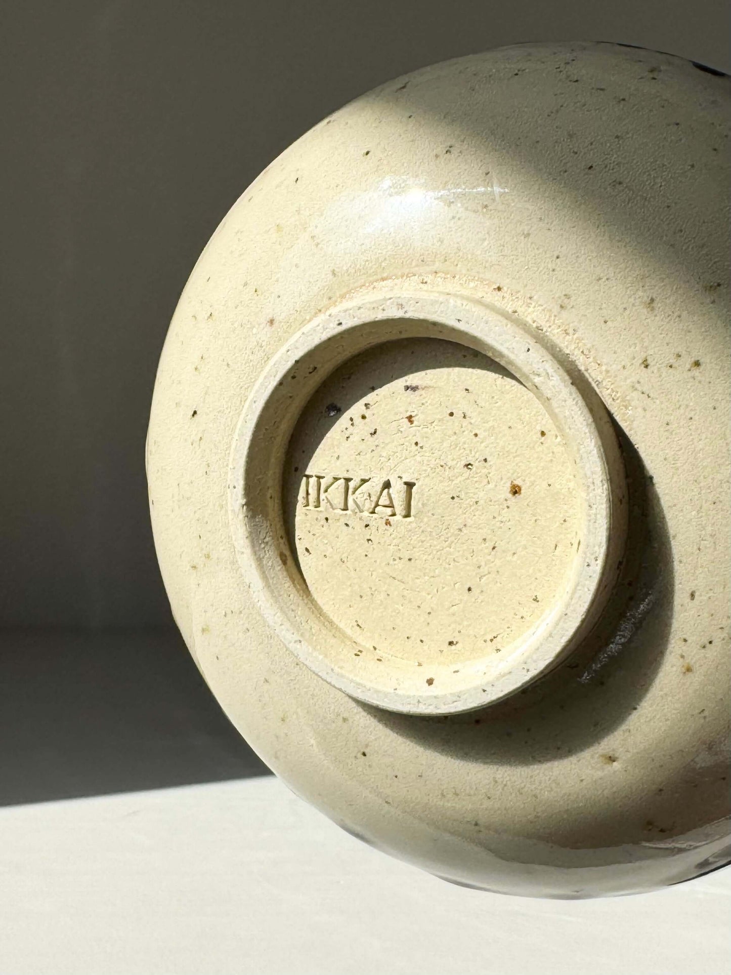 Bottom view of a handcrafted ceramic bowl with a stamped brand name, showcasing a natural, speckled finish in natural light.