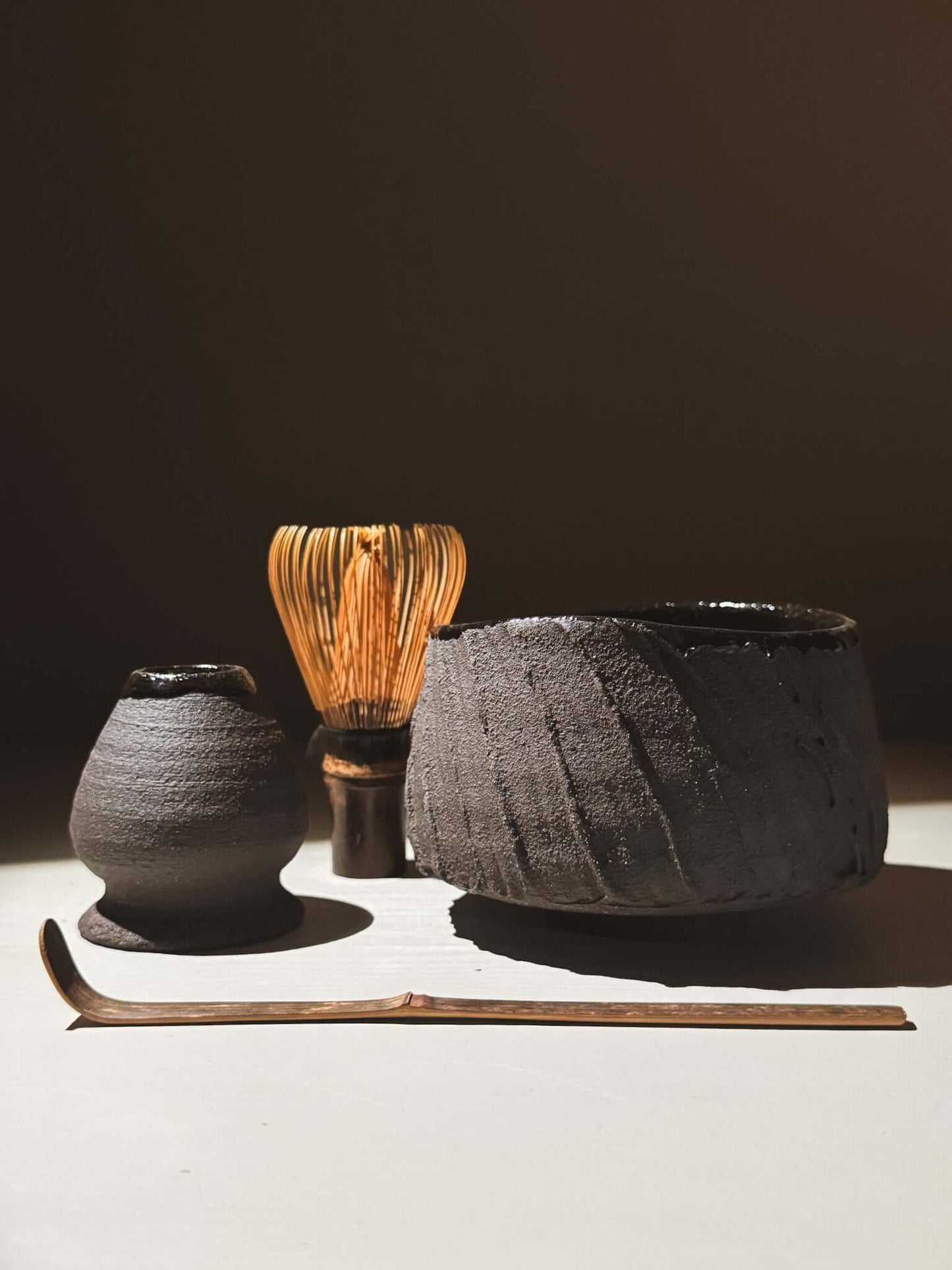 Kuro Matcha Bowl #07 with volcanic stone-inspired textures and dark glaze alongside tea whisk and accessories in natural light.