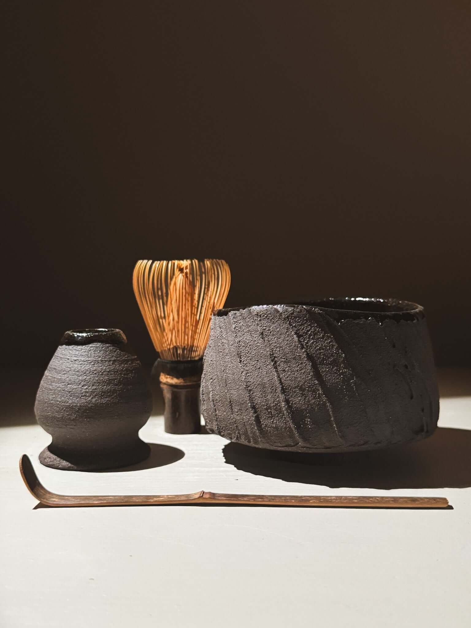 Kuro Matcha Bowl #07 with volcanic stone-inspired textures and dark glaze alongside tea whisk and accessories in natural light.
