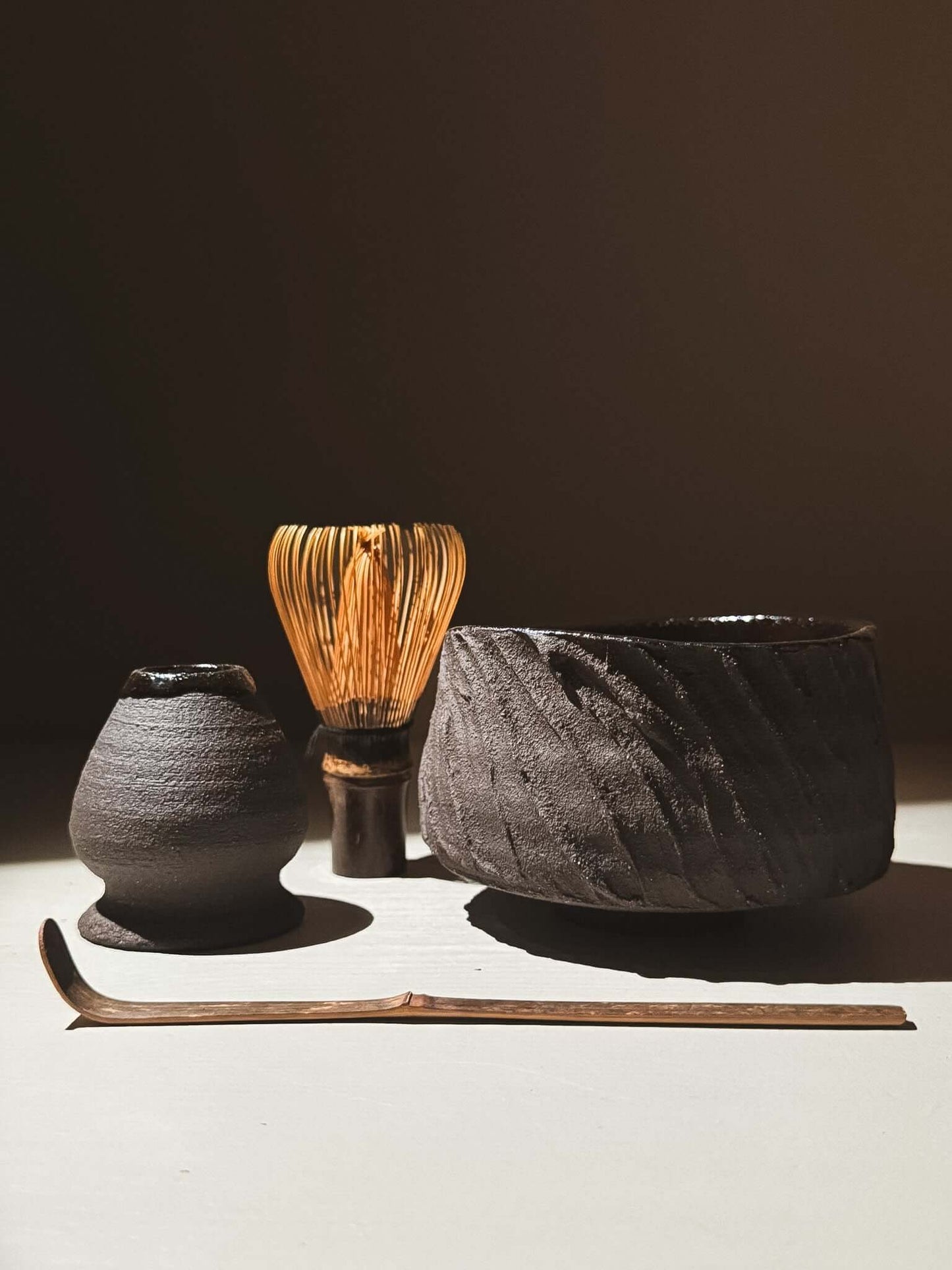 Kuro Matcha Bowl #04 with textured exterior, glossy interior, whisk, and scoop, inspired by volcanic stone and earthy tones.