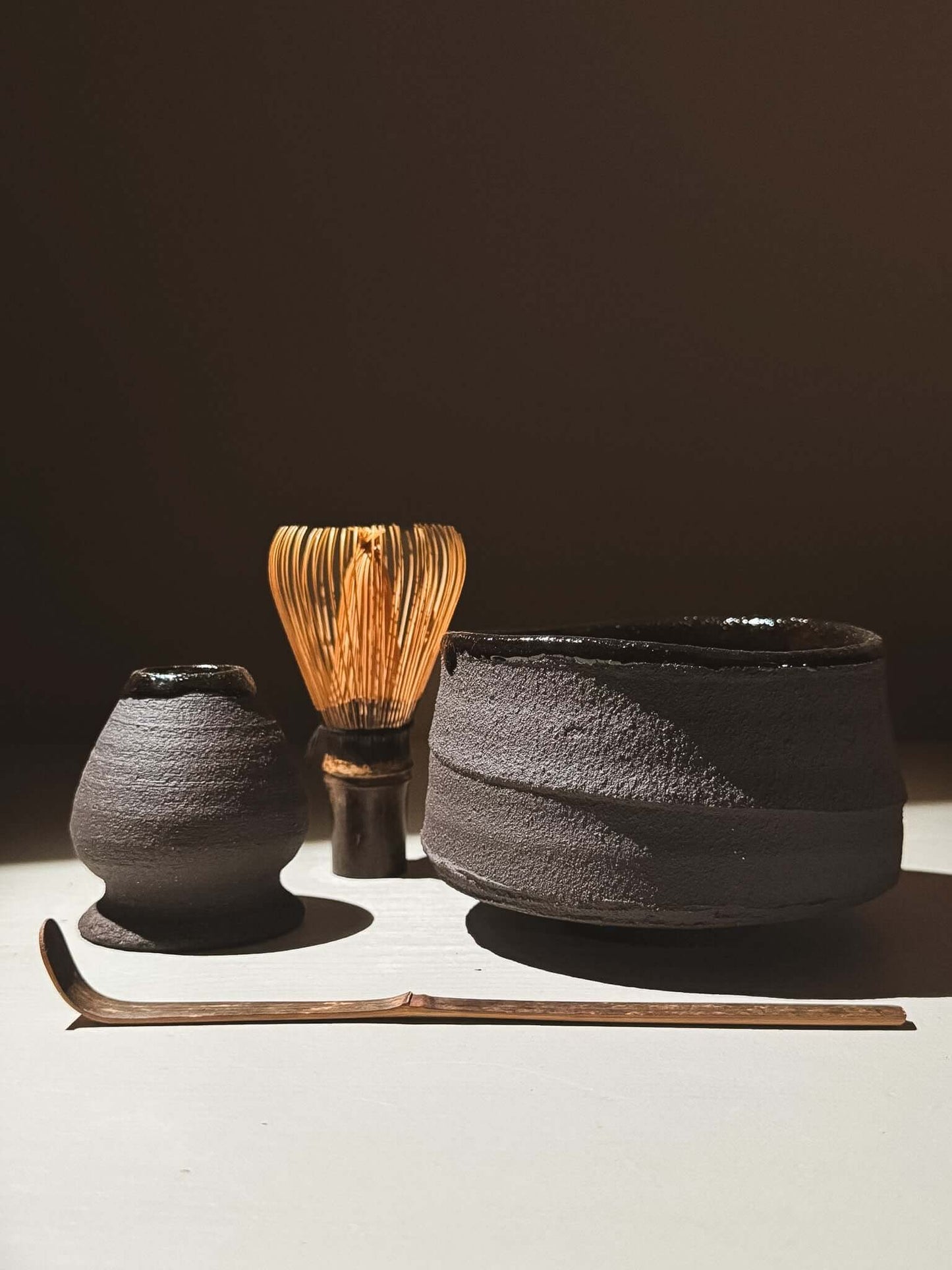 Whisk Holder  - Kuro set featuring dark clay pieces and a bamboo whisk on a light surface.