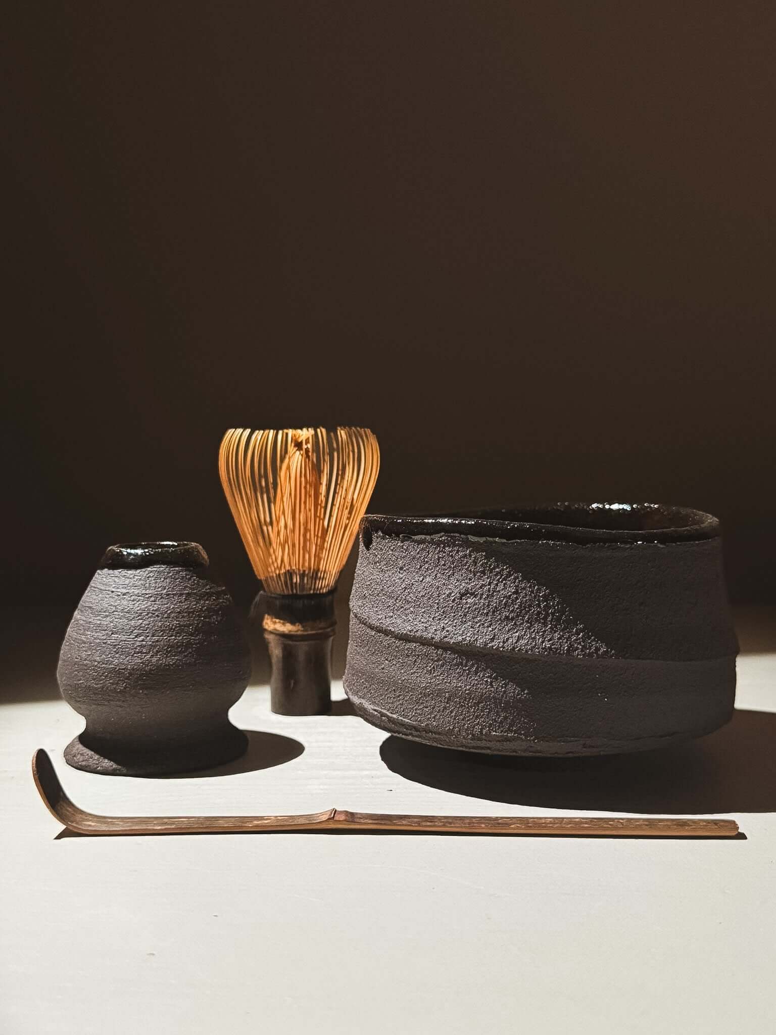 Whisk Holder  - Kuro set featuring dark clay pieces and a bamboo whisk on a light surface.