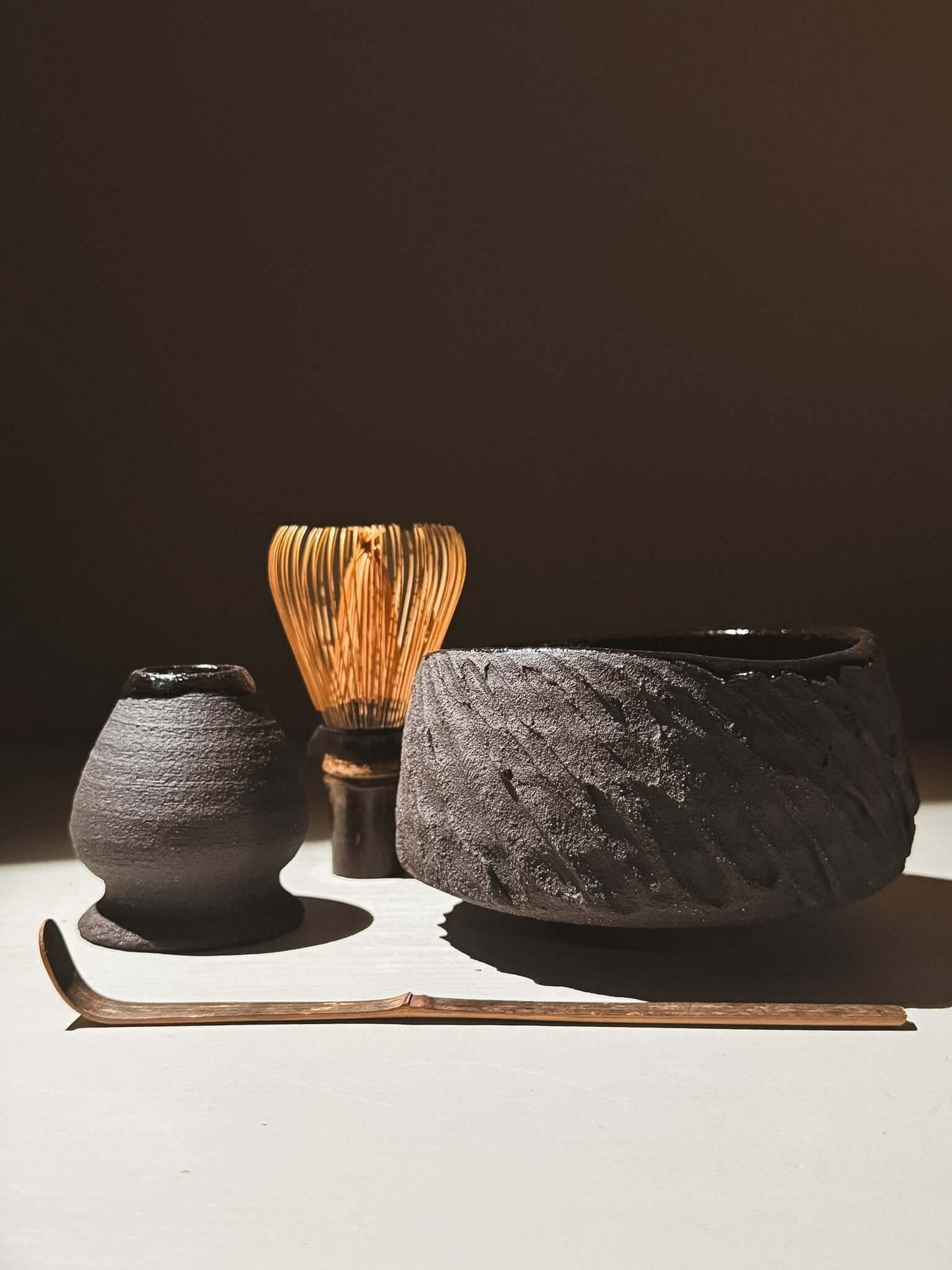 Kuro Matcha Bowl #08 with volcanic stone texture and dark glaze, surrounded by traditional matcha tea tools on a neutral background.