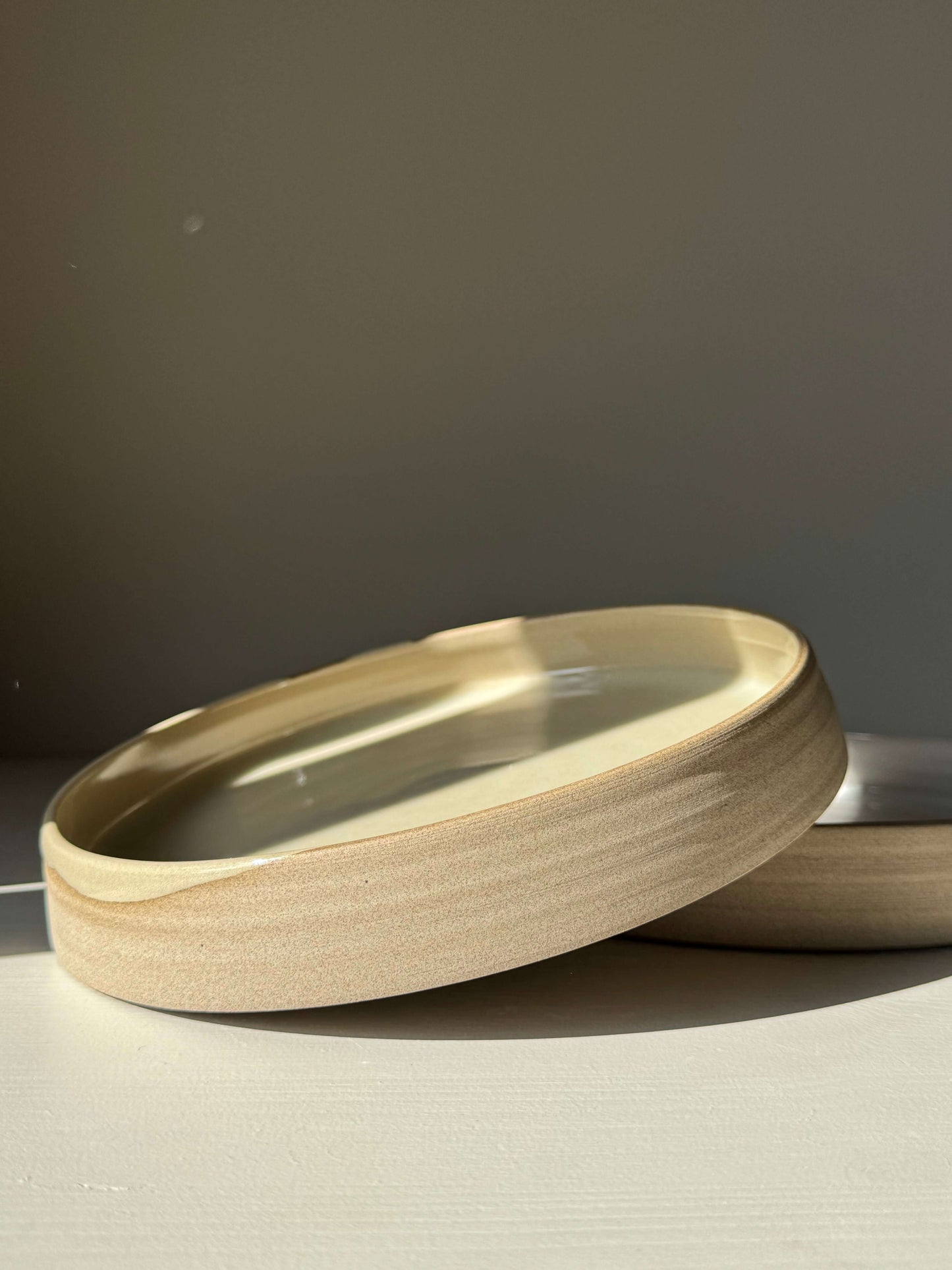 Large Plate – Inyo: Handmade ceramic plate with glossy clear glaze and raw clay edge, showcasing reflective surface and unique design.