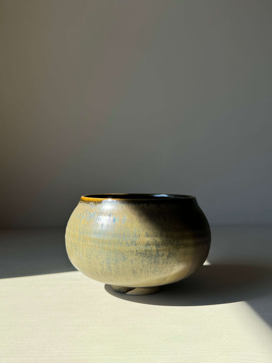 Sabi Black matcha bowl with soft black glaze and golden ochre tones, inspired by wabi-sabi, set against a neutral background.