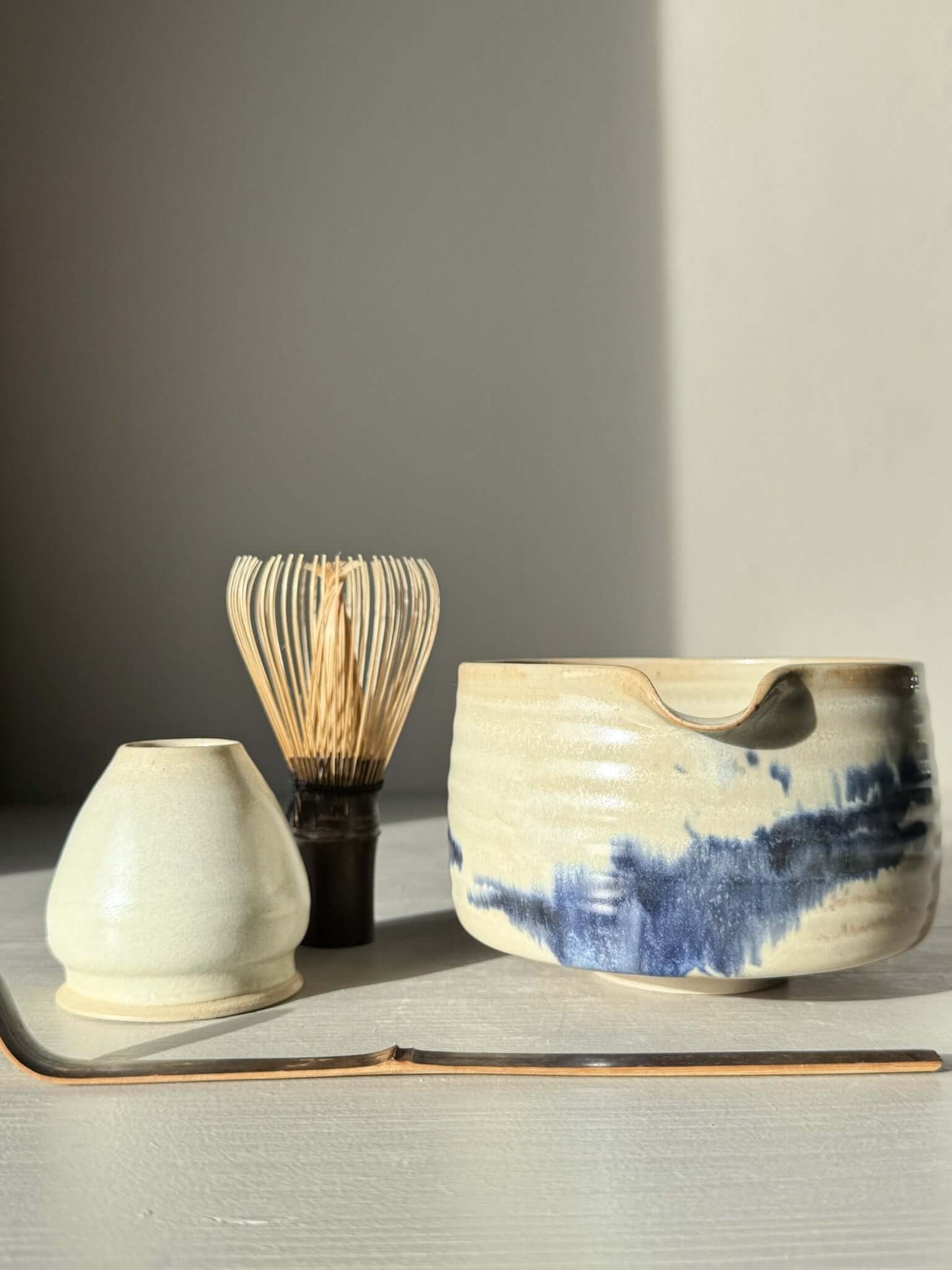 Matcha bowl Spout - Moonstone & Blue #03 with hand-splashed cobalt glaze beside matcha whisk and scoop on a tabletop.