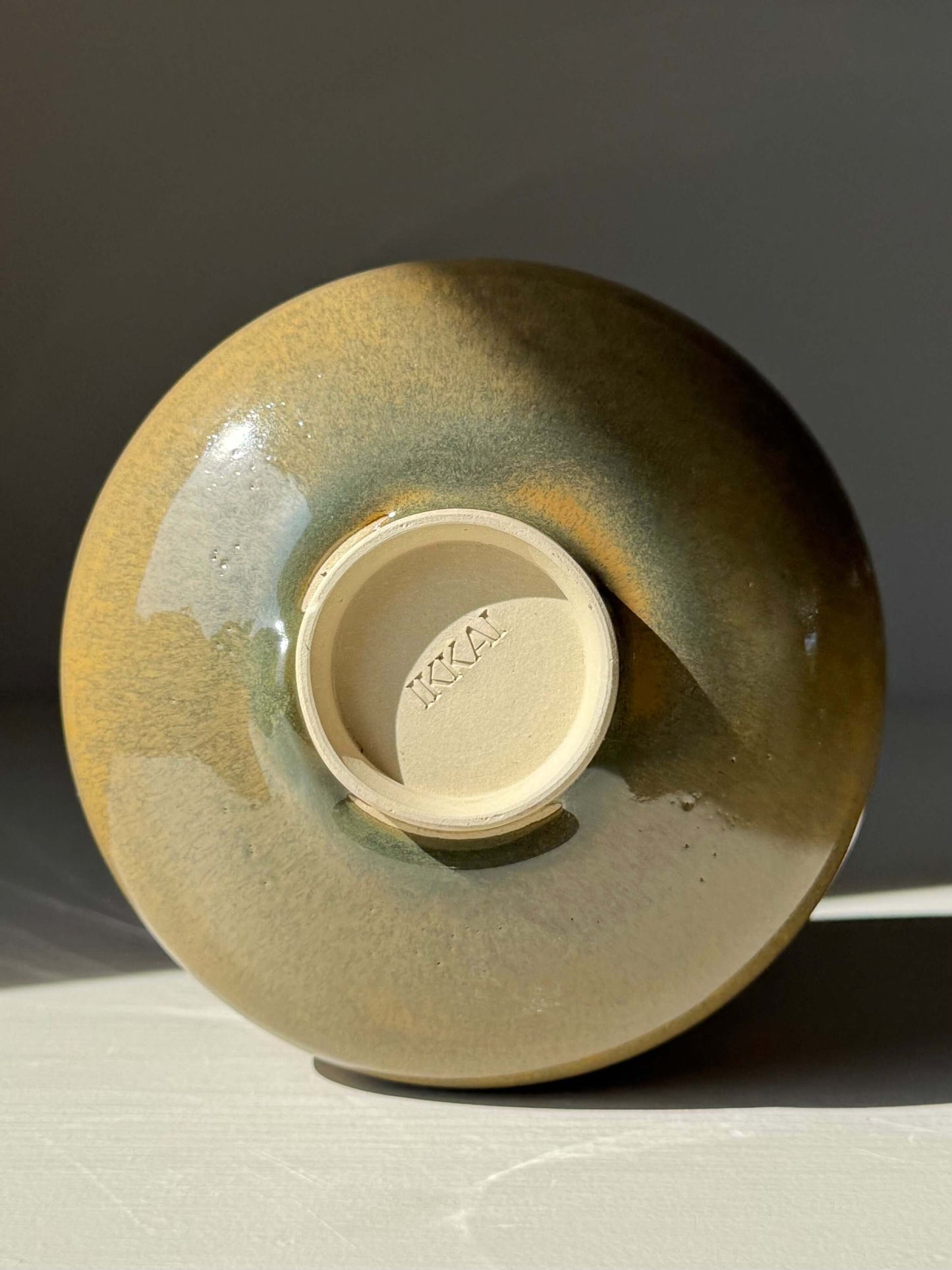 Bottom view of a handmade ceramic Matcha Bowl – Tenmoku Glaze, showcasing its rich, glossy finish in light and shadow.